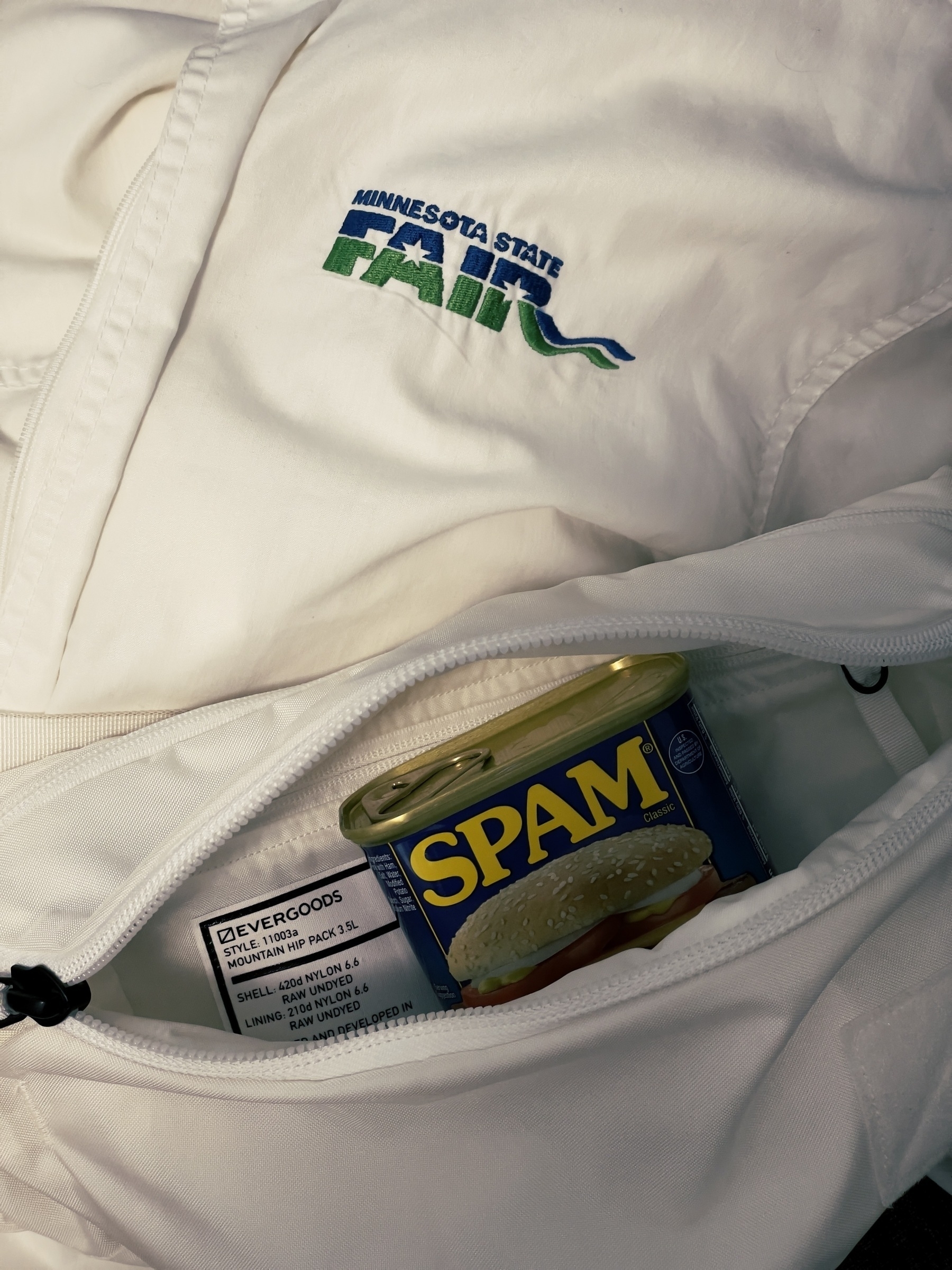 Openened white sling bag with can of SPAM inside, next to a Minnesota State Fair jacket