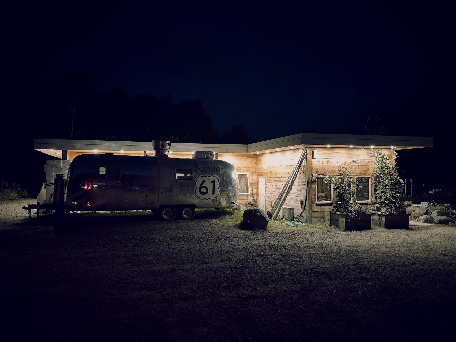 Exterior of a Nordic/wooden restaurant building at twilight with a silver food cart trailer parked against the lit backdrop, with a Scenic 61 logo imprinted on it.