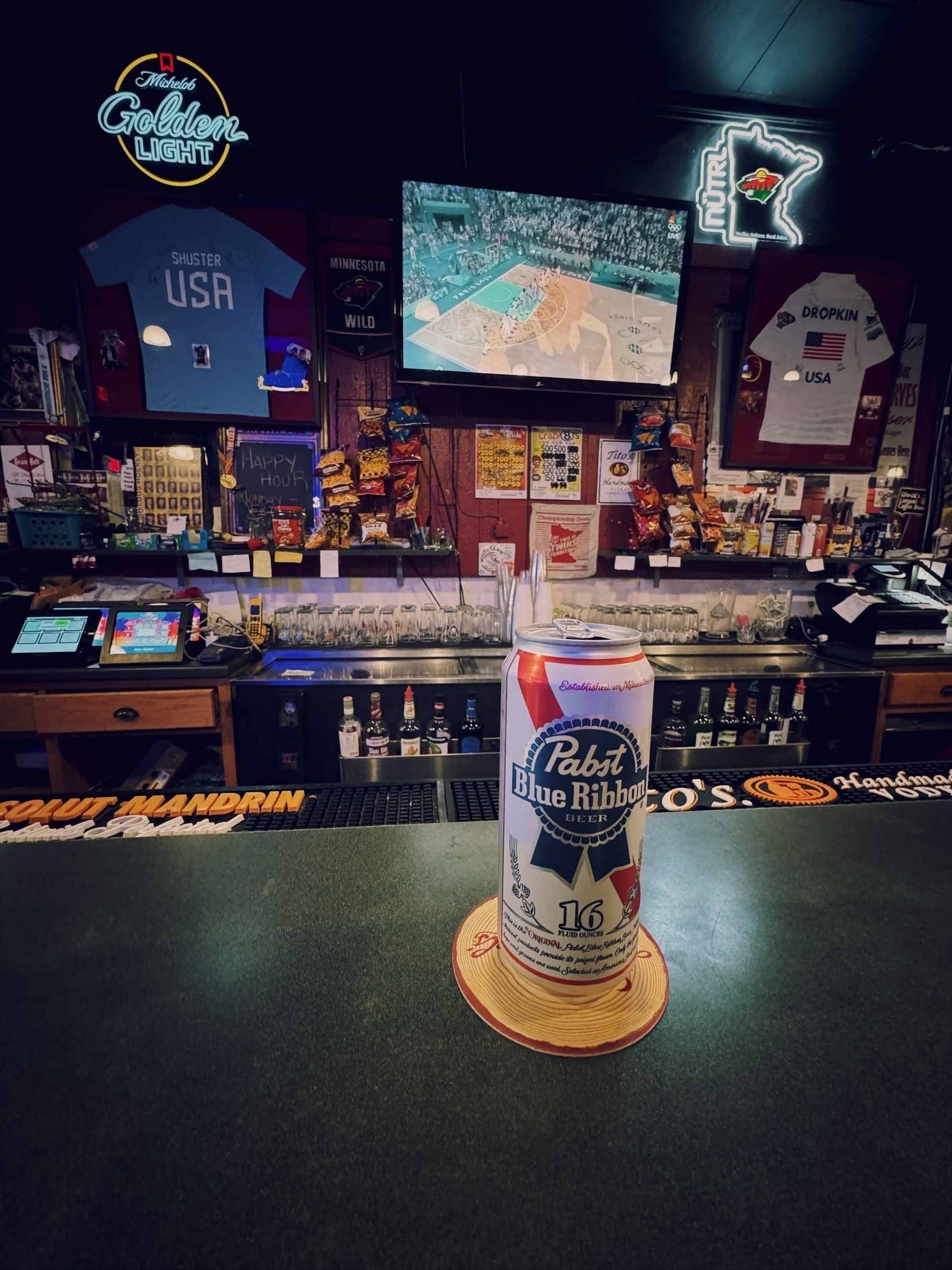 PBR can on bar top in front of dive bar wall with TV and Olympics basketball on