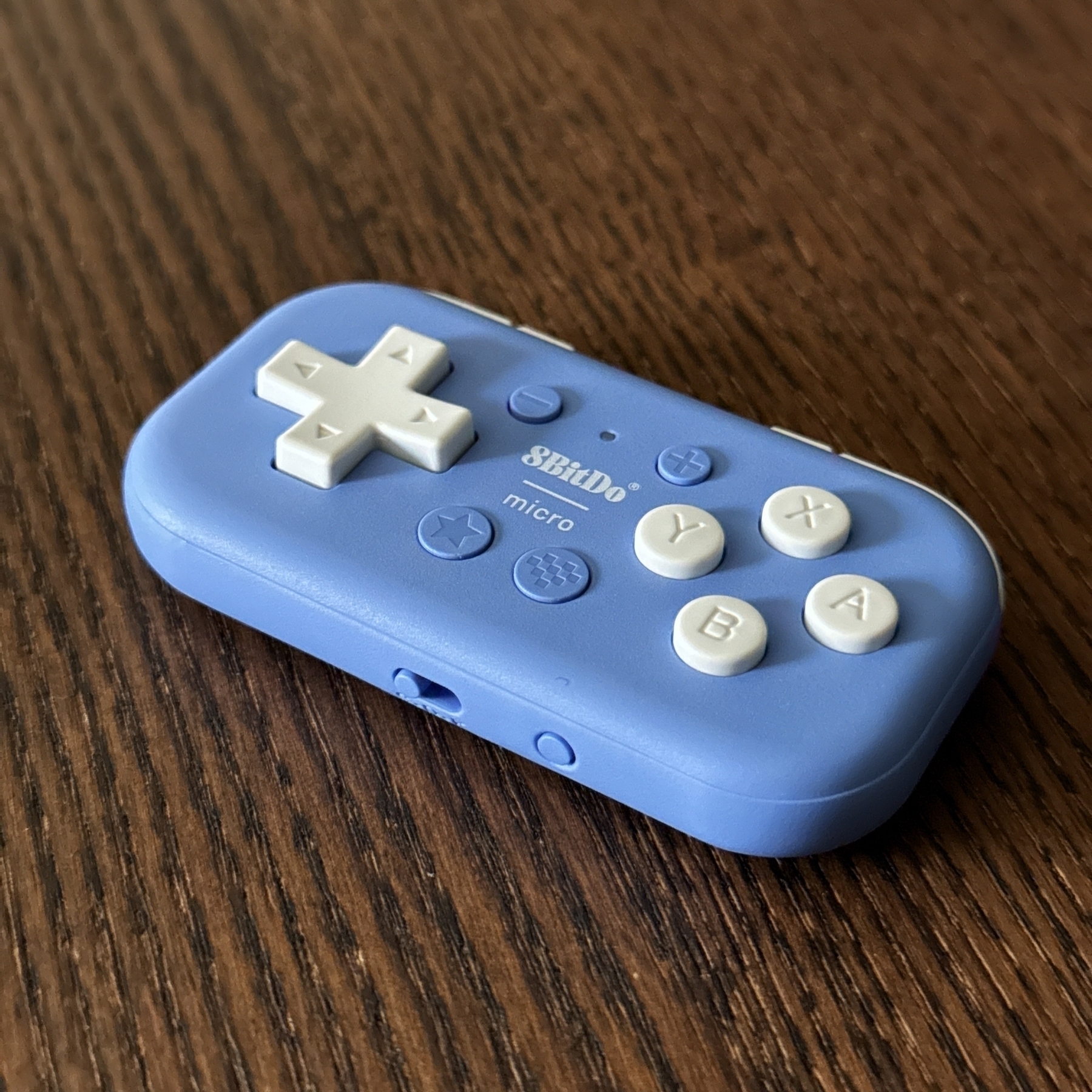 A small rectangular controller in a shade of purple-blue sitting on a dark wooden surface