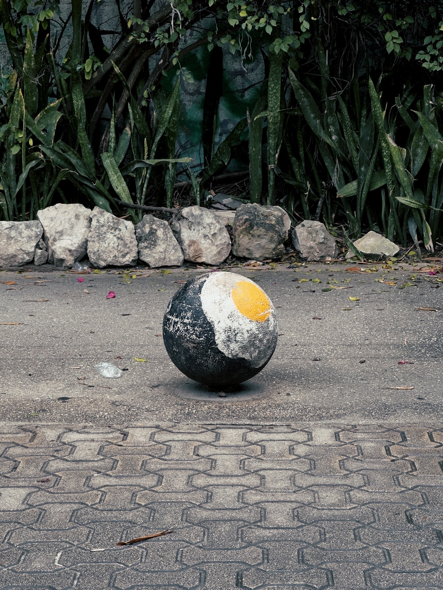 Egg painted on black concrete ball, sitting on a tiled sidewalk