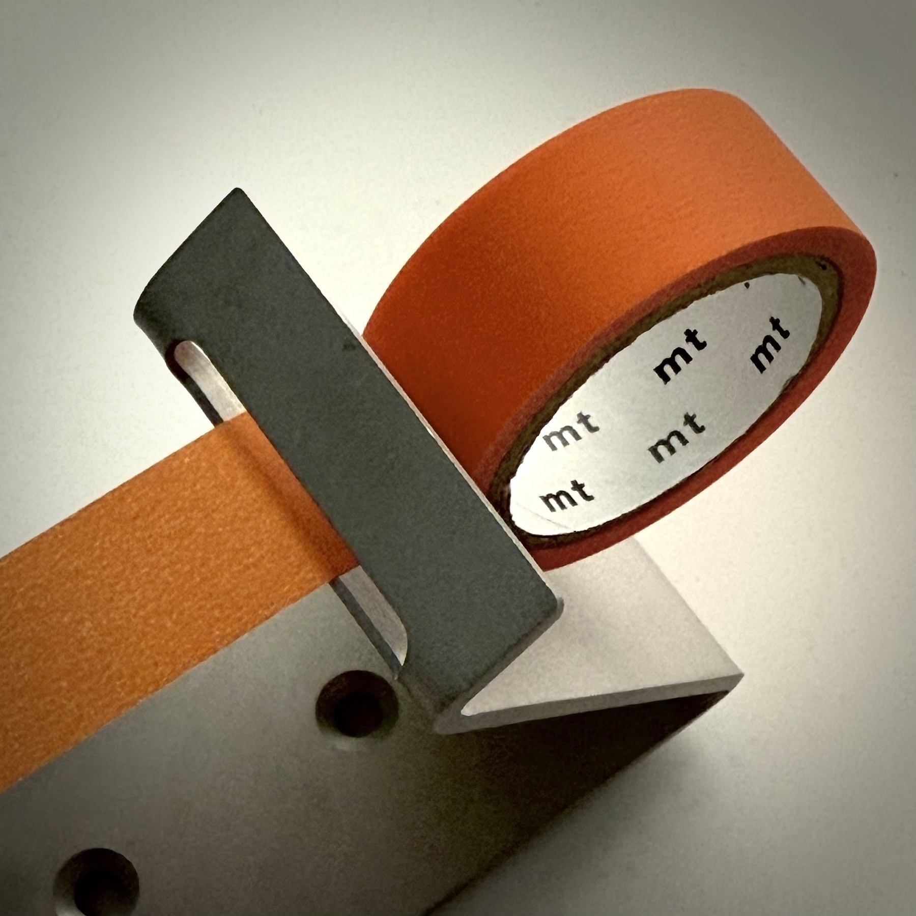 Closer view of an orange roll of tape attached to a metal mechanism that holds it