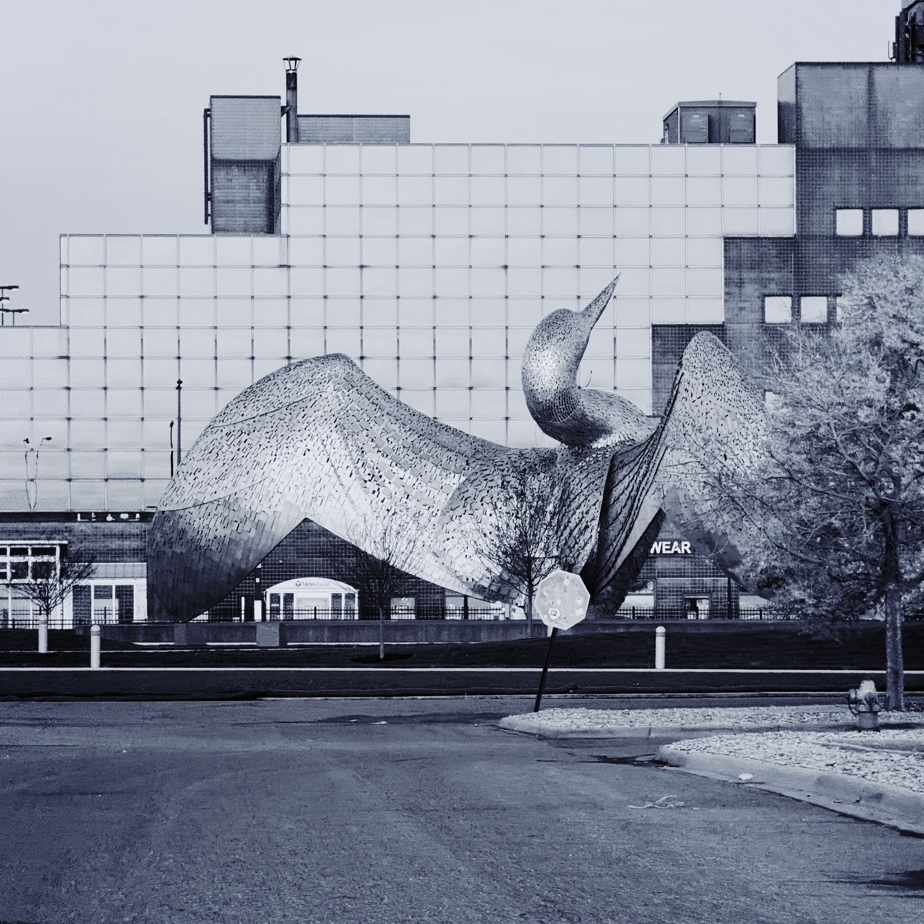 black and white photo of the rear of a giant loon statue in front of a glass-windowed building