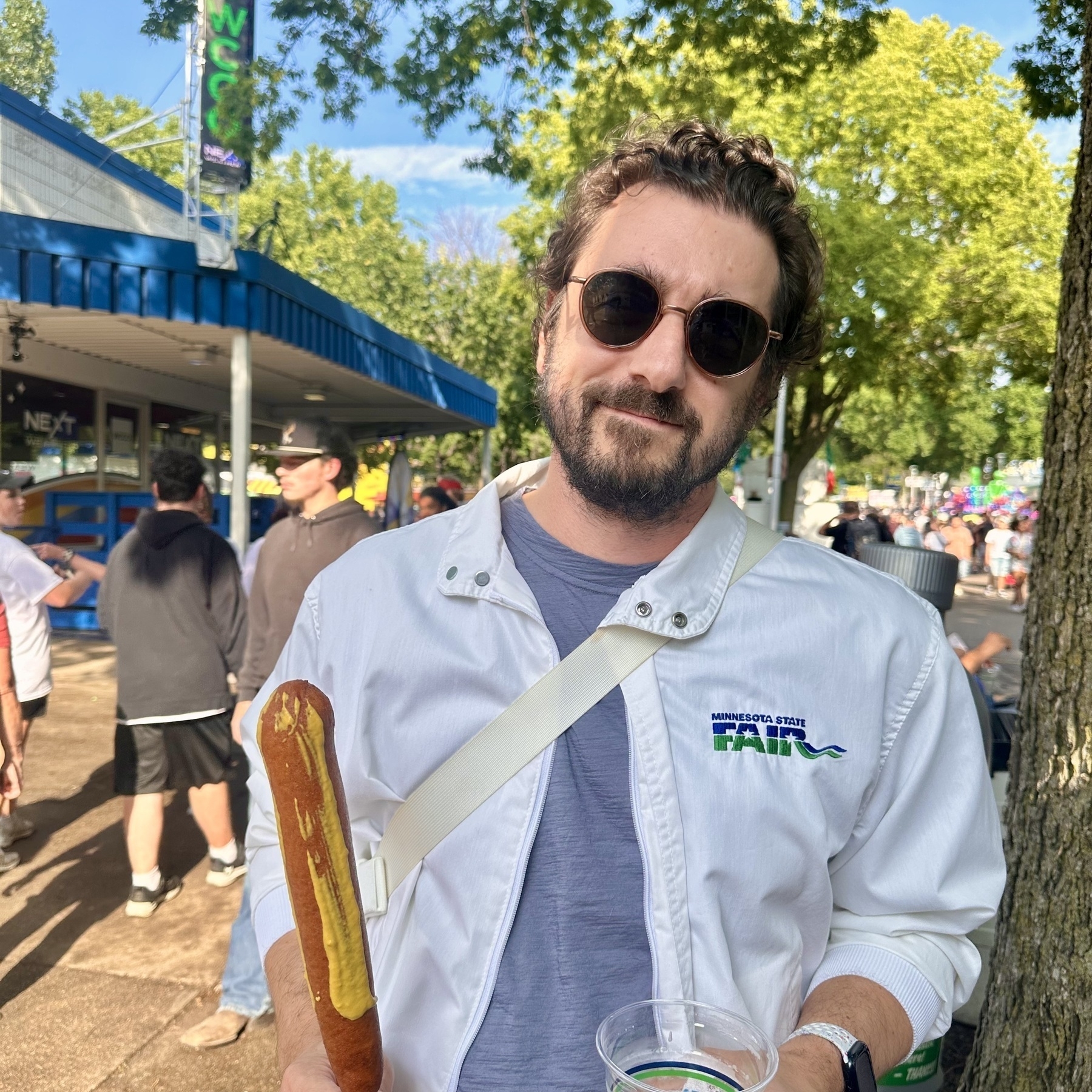 image of the author in a white State Fair jacket and mustard-dressed pronto pup in hand with a beer