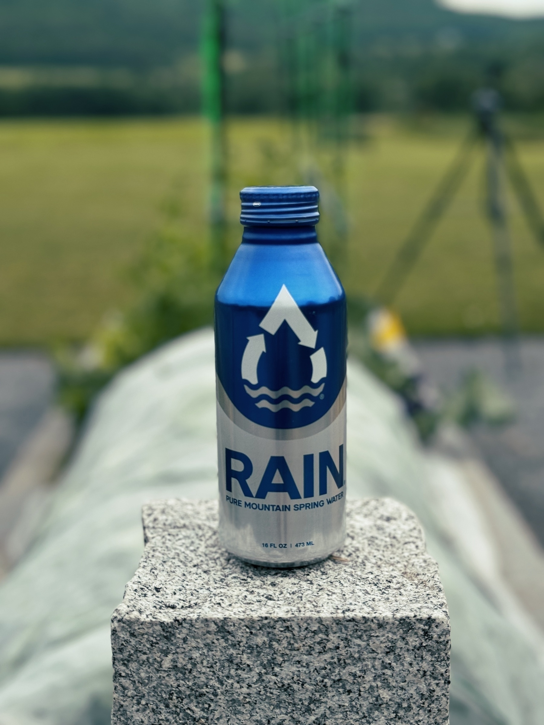 aluminum bottle of water with blue colorway atop a stone pillar in front of a farm blurred in the background
