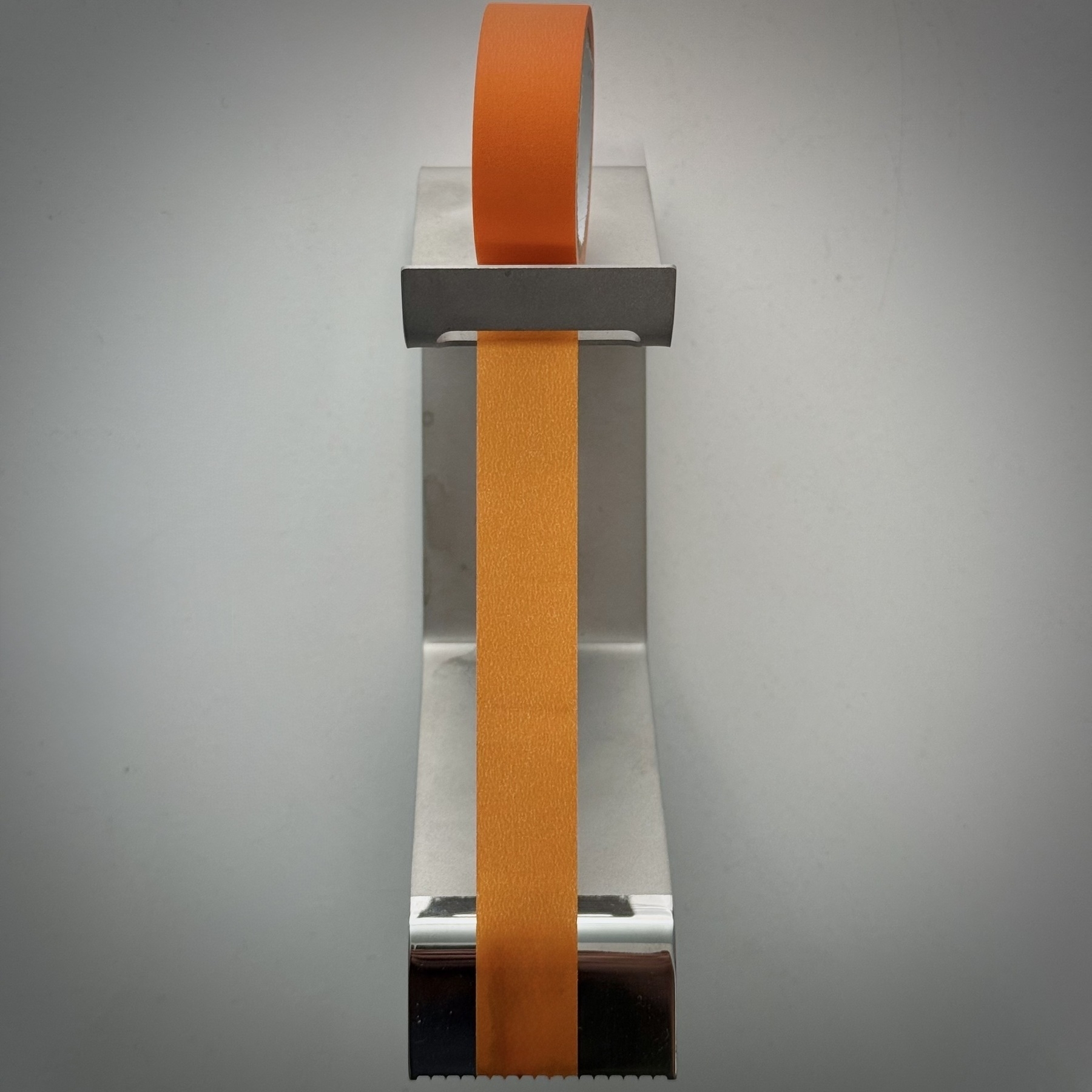 Top down view of a metal object holding at the rear an orange roll of masking tape