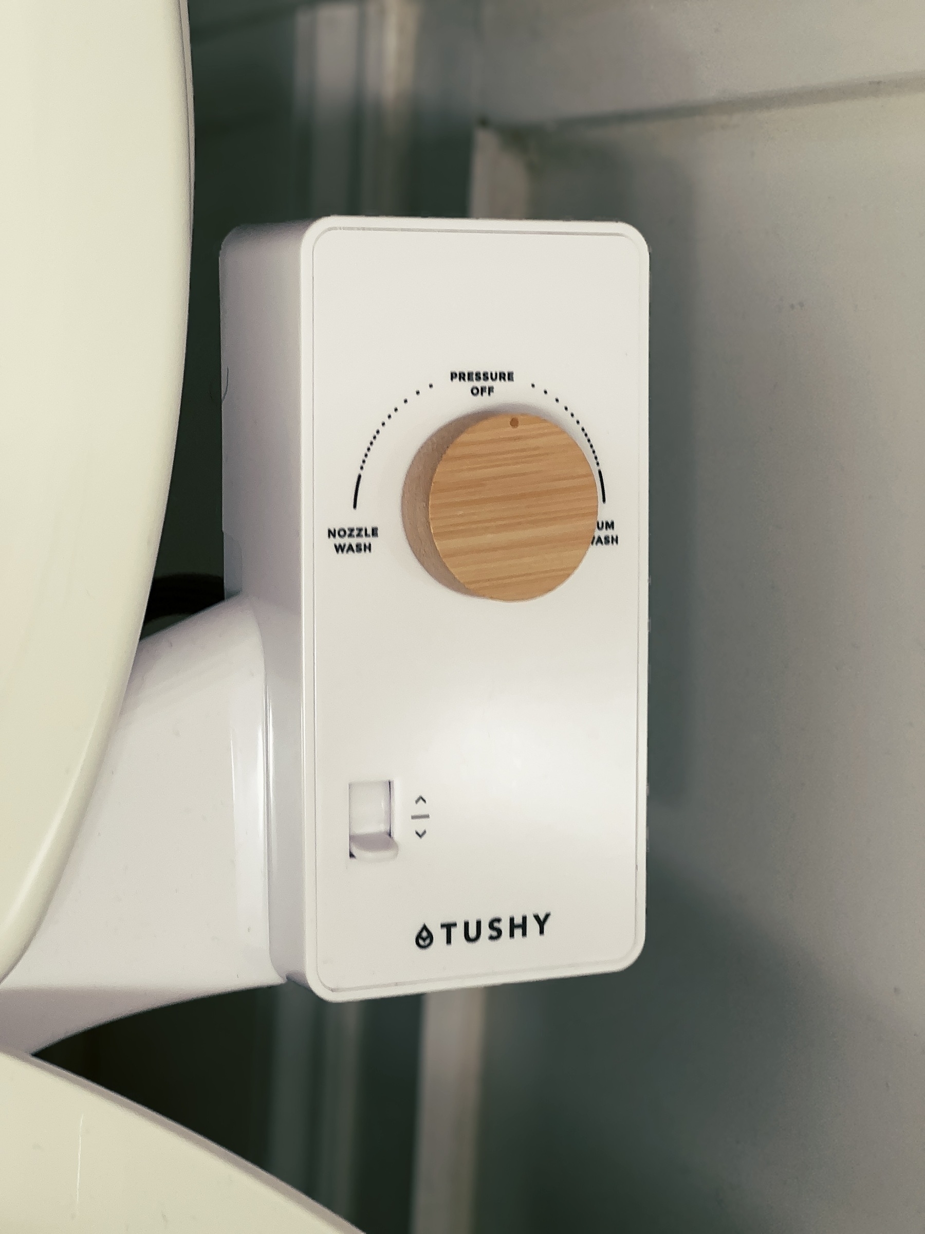 a white wand-only bidet attached to a toilet with the branding Tushy visible, along with a wooden turn-dial control