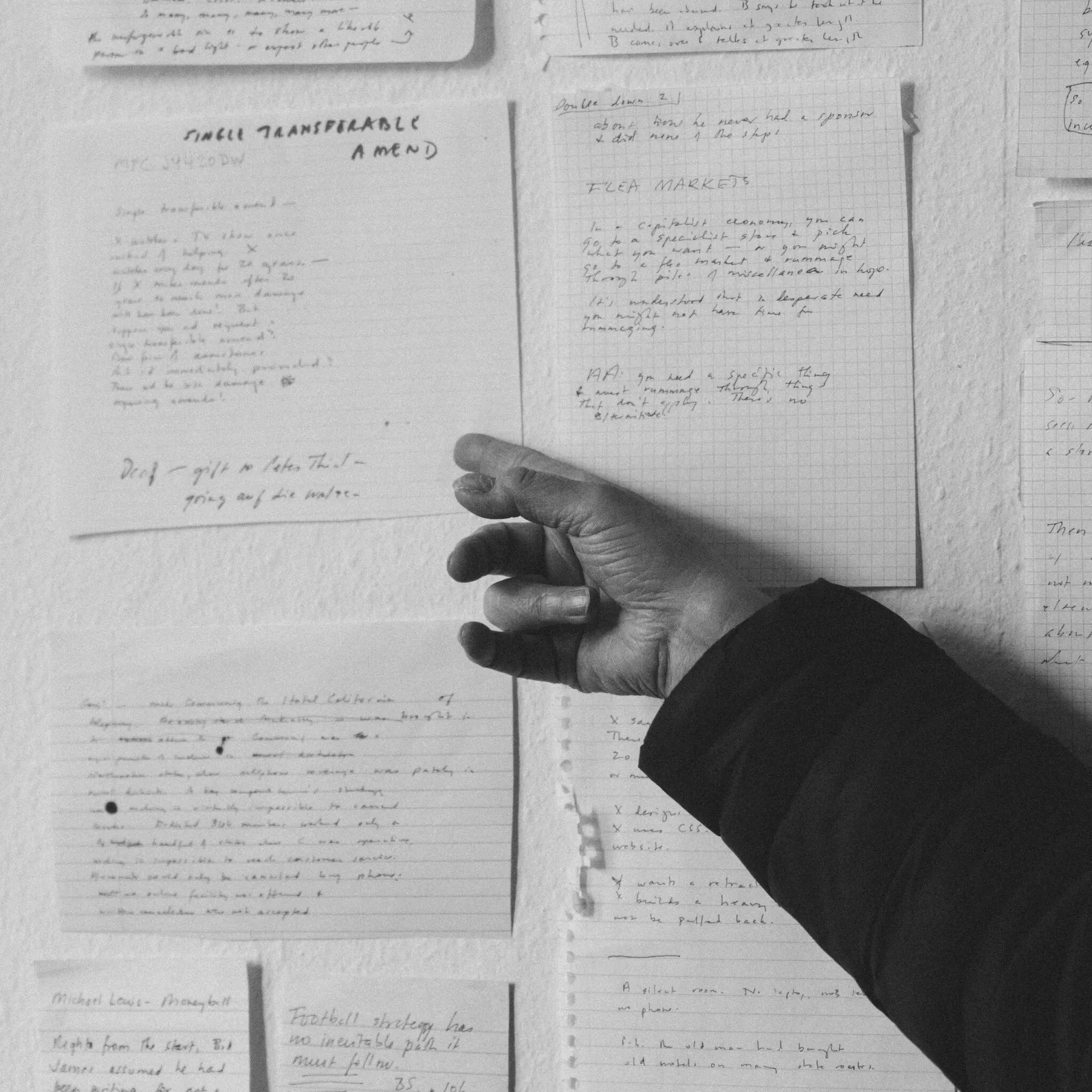 A person's hand points at handwritten notes pinned to a wall. (image by Mustafah Abdulaziz for The New York Times)