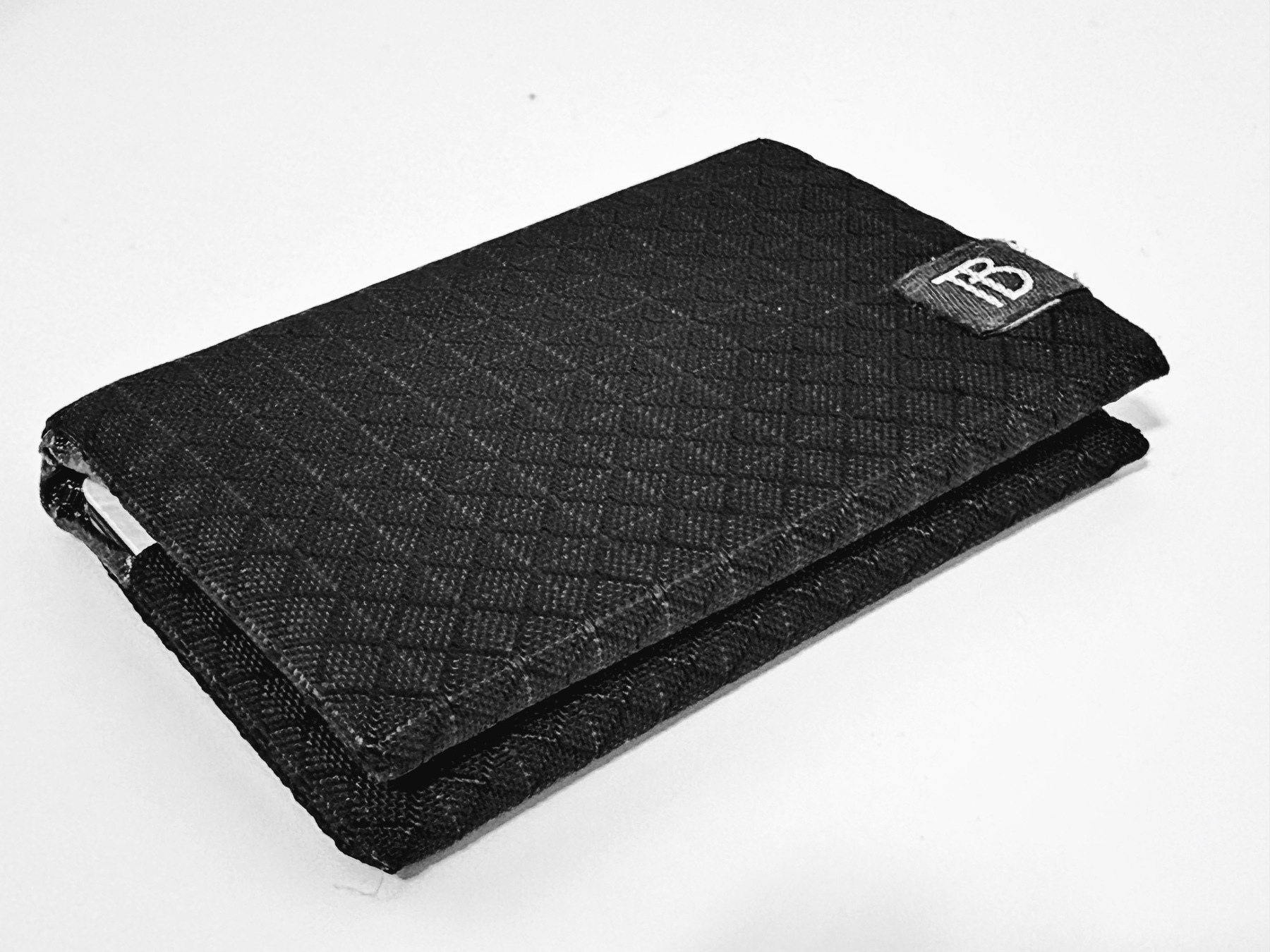 A black textured wallet with a small logo in the corner lies on a white surface.