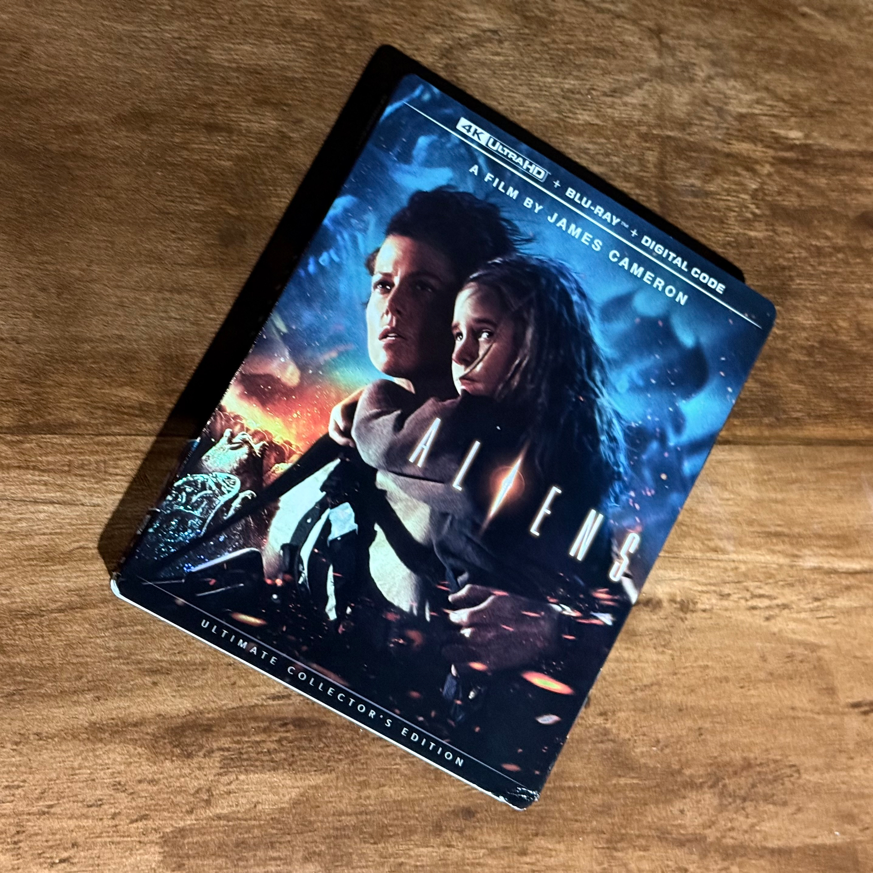 A 4K UltraHD edition of the movie Aliens directed by James Cameron is shown resting on a wooden surface.
