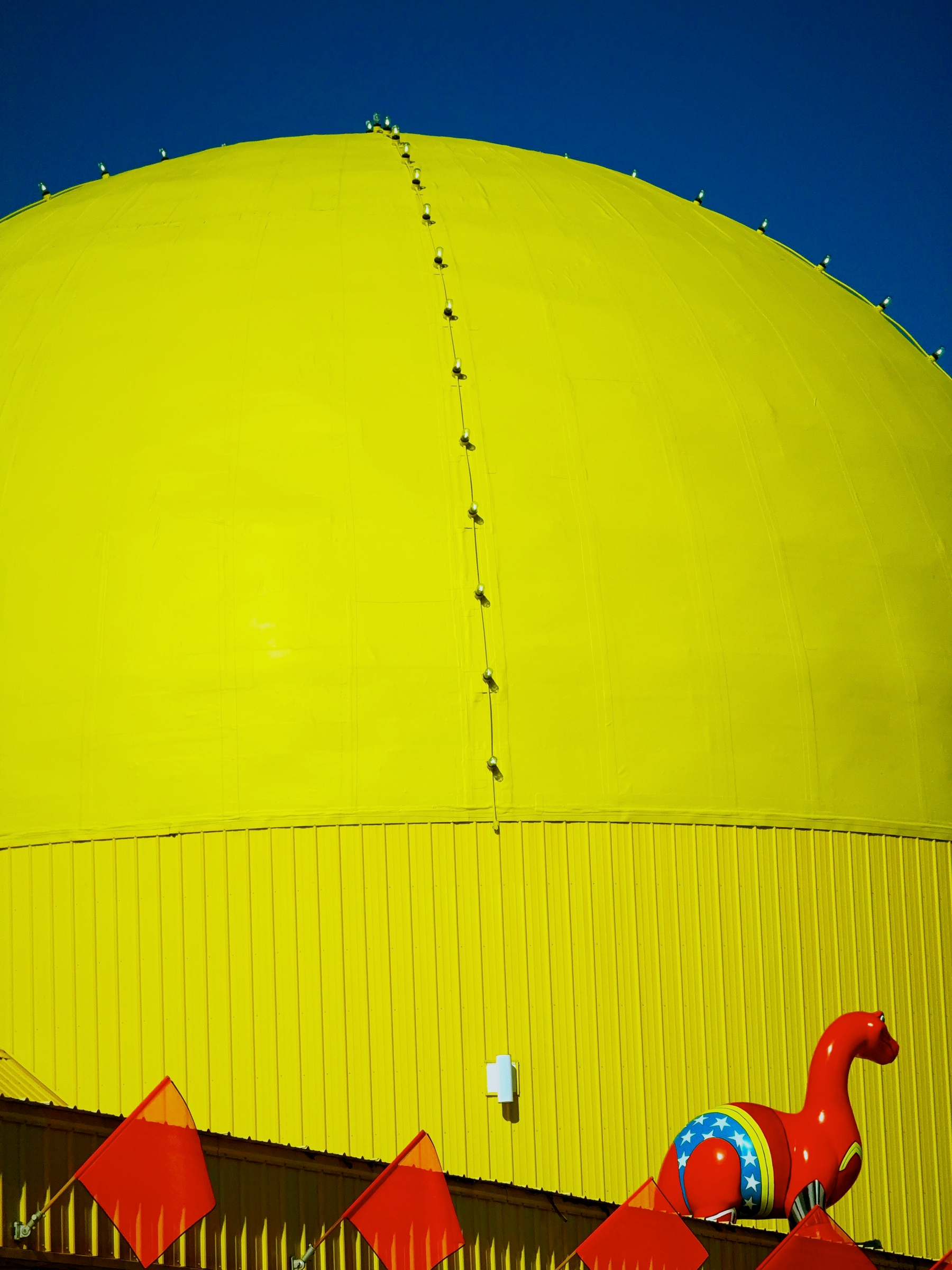 A large yellow spherical structure with a red decorative dinosaur and red flags positioned in front of it against a clear blue sky.