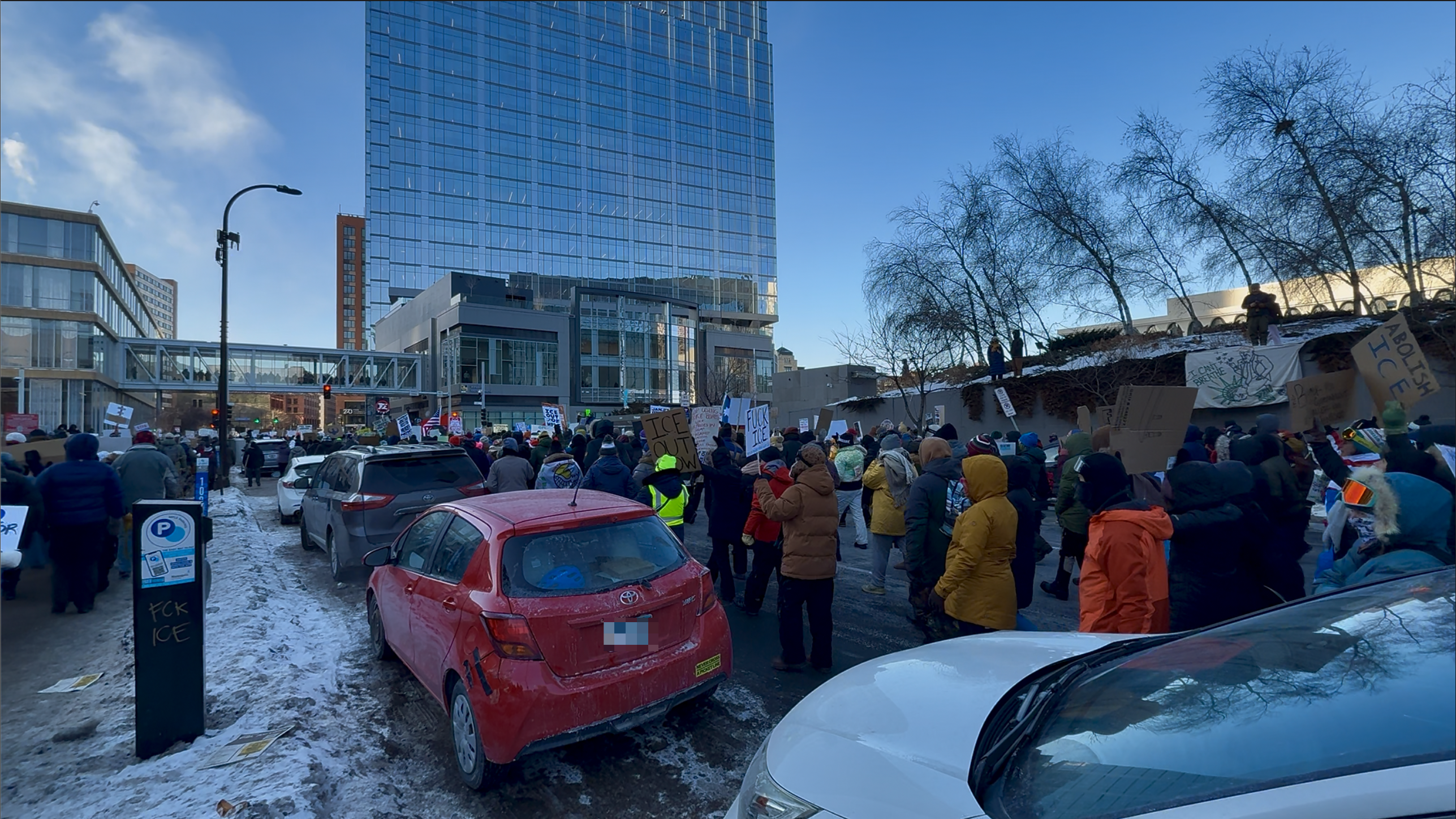 A crowd of people is gathered on a snowy street holding signs in front of a tall building.