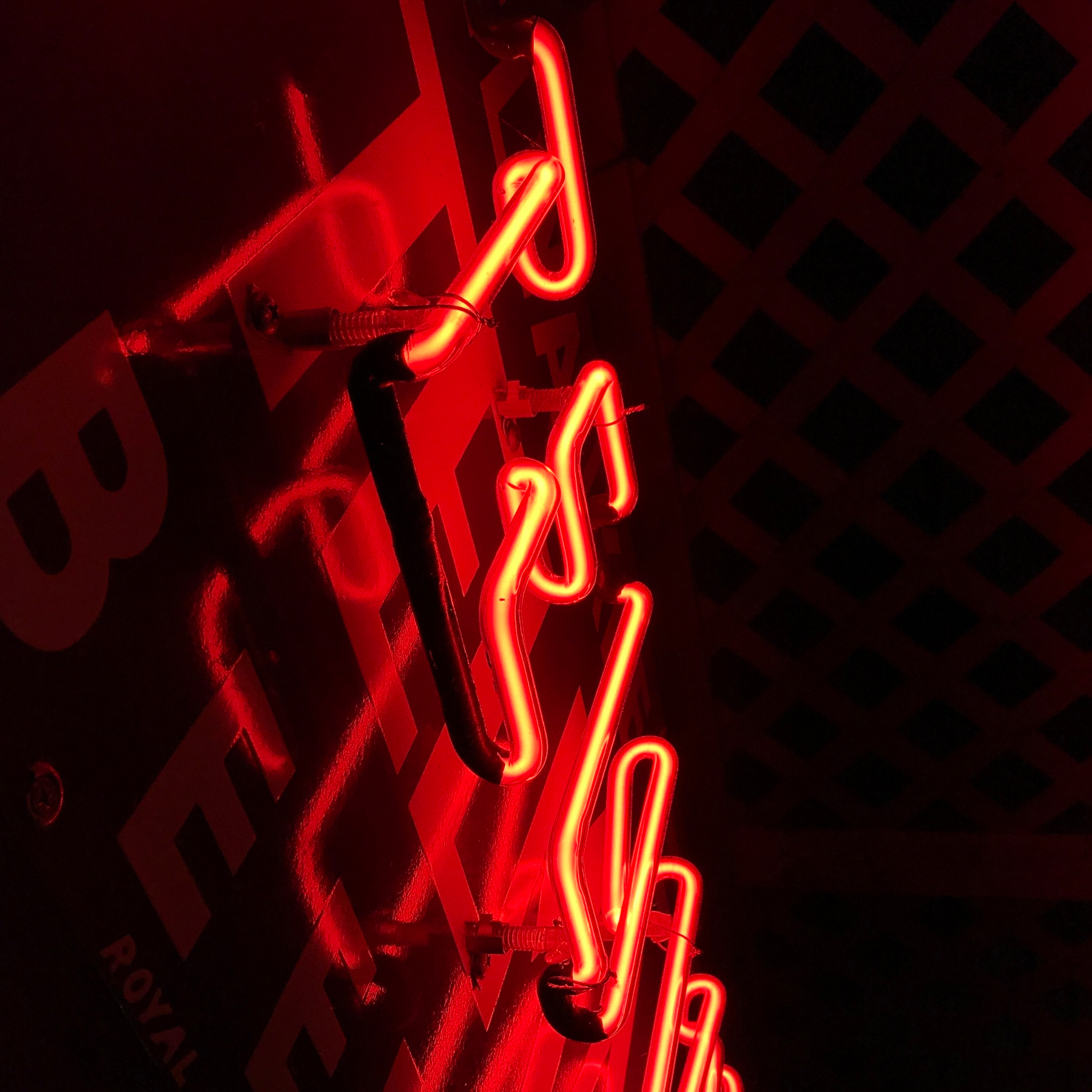 A red neon sign is mounted on a wall with a lattice pattern above it.