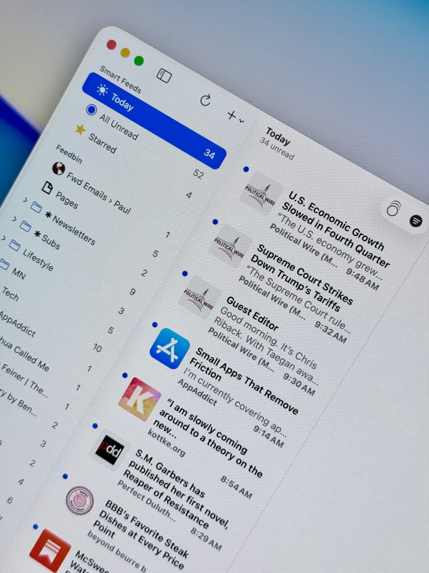 A digital interface (NetNewsWire Mac app) shows a list of RSS feeds with subject lines and previews, including topics like economic growth, Supreme Court decisions, and various articles.