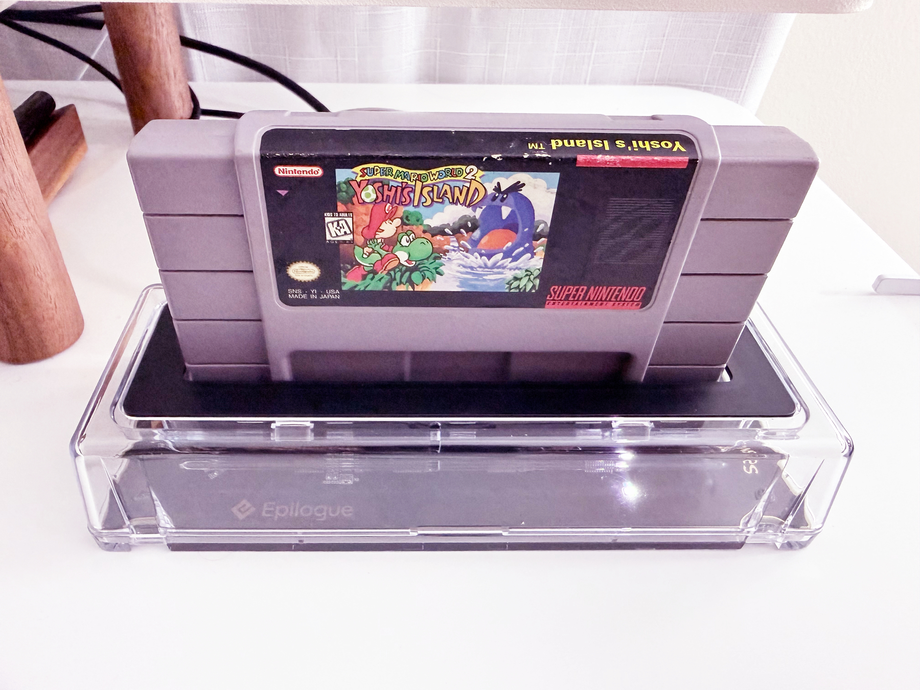 A translucent hardware device with a Super Nintendo cartridge Yoshi's Island inserted on a white desk