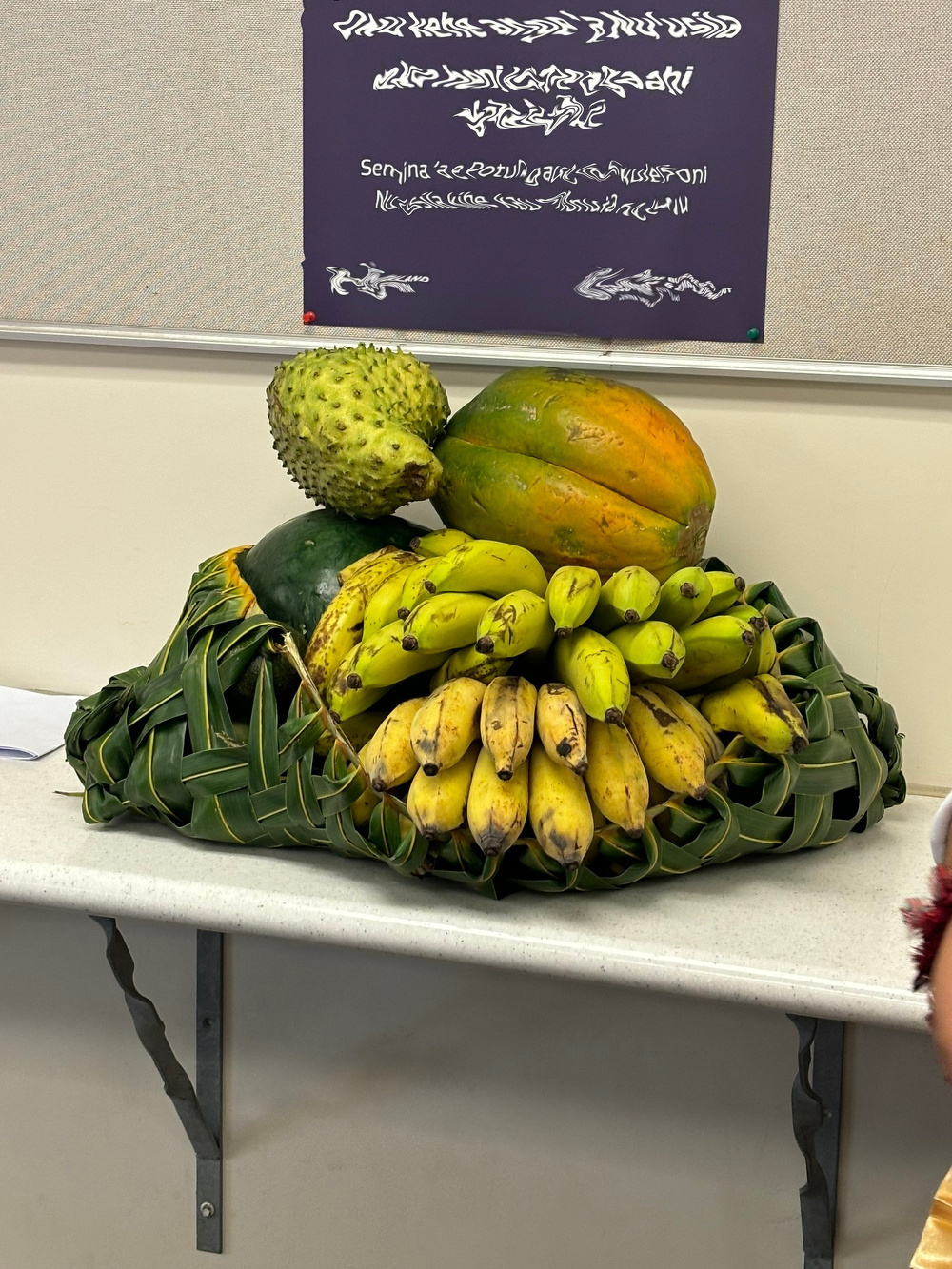 A display of bananas, papaya, and other tropical fruits is arranged on a table with a decorative leaf base.