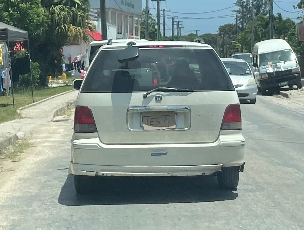 A white Honda minivan is on the road with a makeshift cardboard license plate reading TEST.
