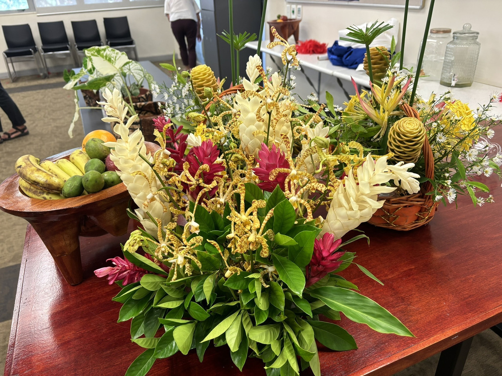 A vibrant display of assorted flowers and tropical fruits is arranged on a wooden table.