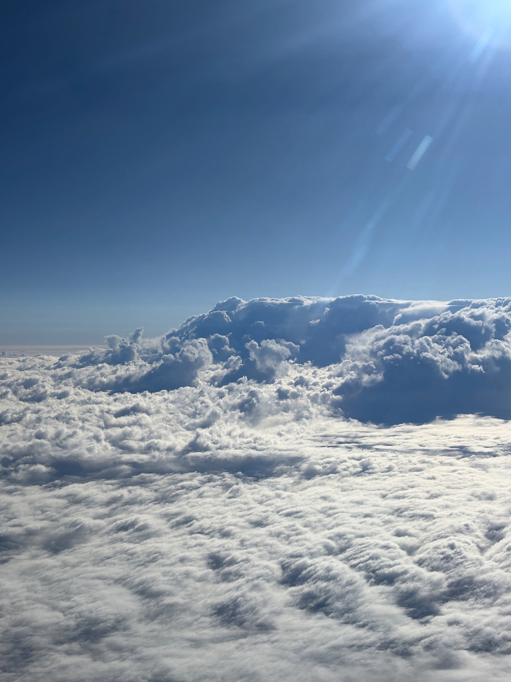 A breathtaking view of a cloudscape with sunlight streaming over a vast expanse of fluffy clouds and blue sky.