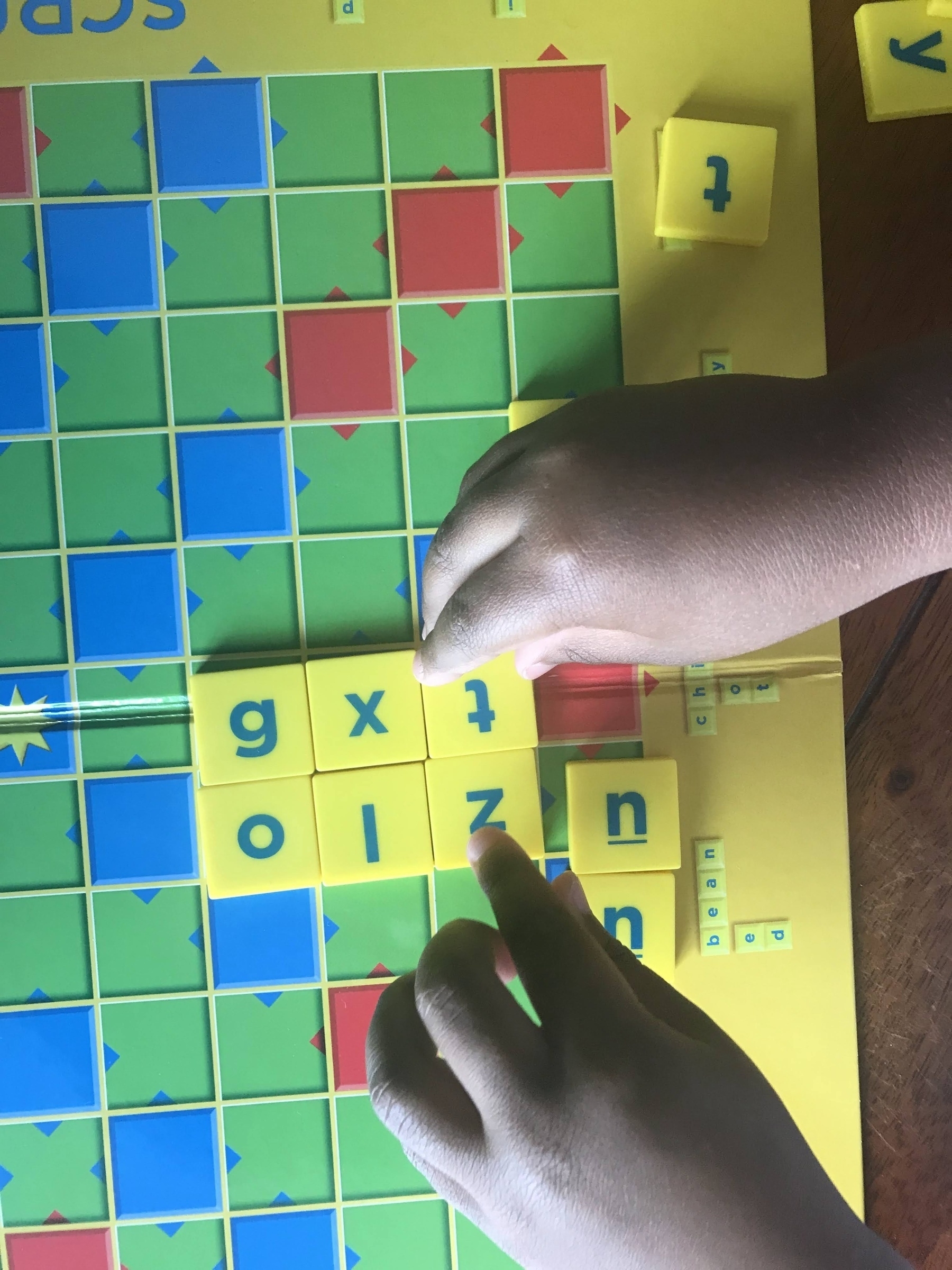 Three year old hands placing Scrabble pieces spelling "oizn"