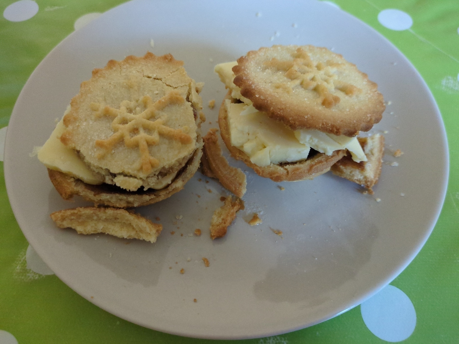 Two shop bought mince pies on a plate after being warmed in the oven, decapitated and topped with cheese, lids back on again. All slightly dilapidated.