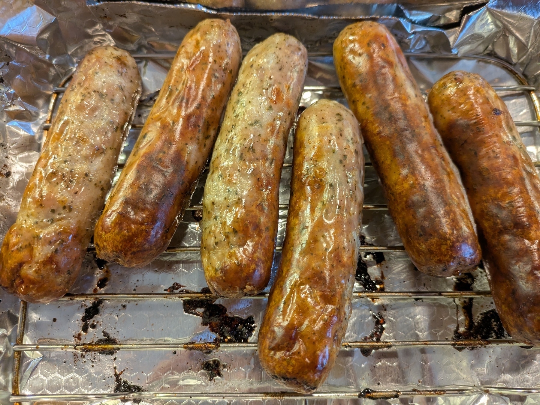 Six cooked Lincolnshire sausages sizzling on a baking tray