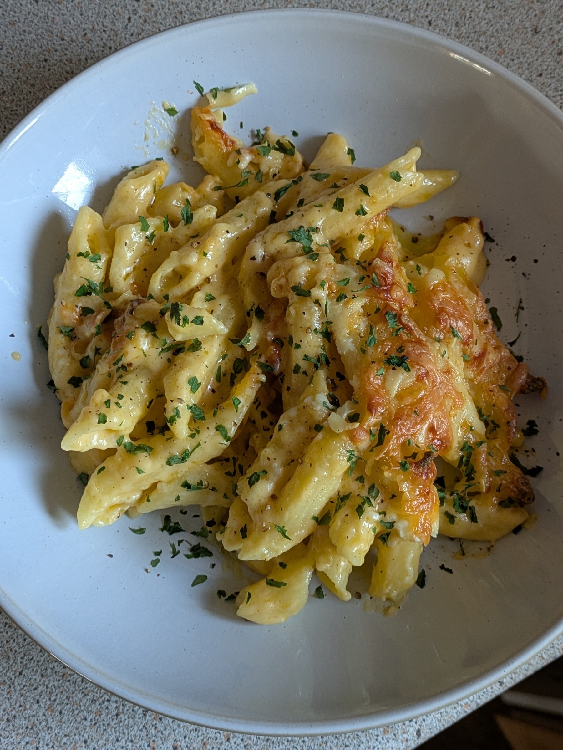 A plate of cheesy penne pasta is garnished with parsley.