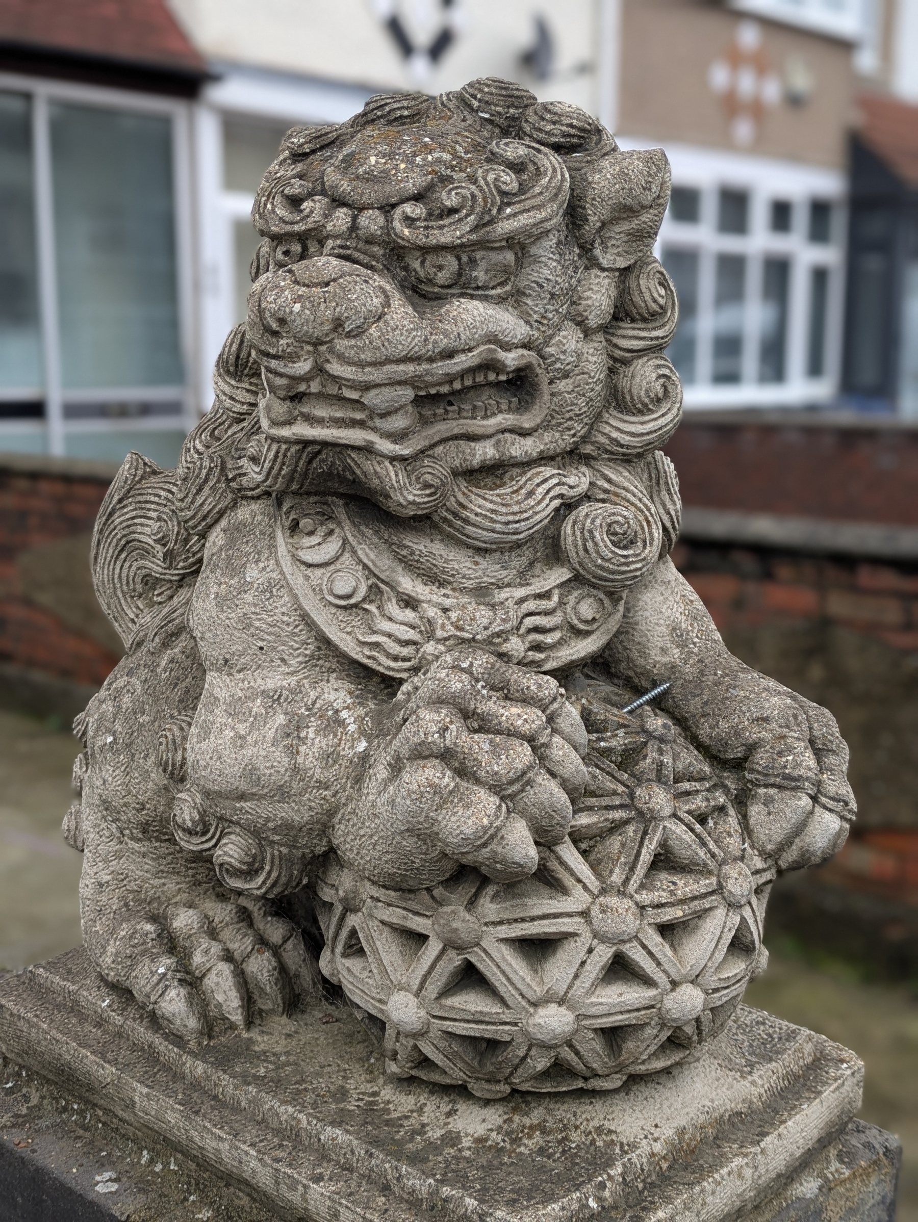 A stone sculpture depicts a traditional guardian lion holding a decorative orb outdoors.