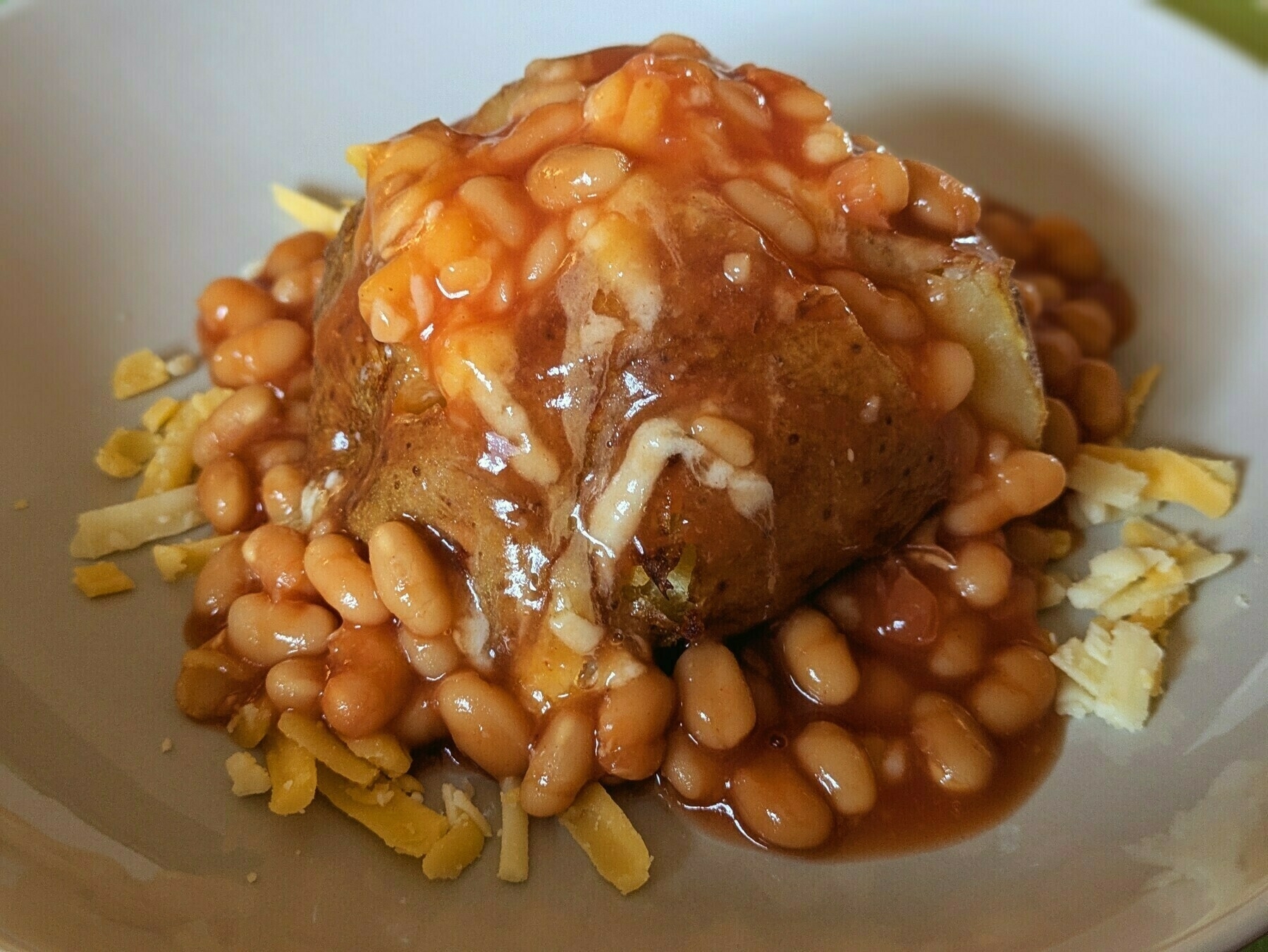 A baked potato topped with baked beans and melted cheese is served on a plate.