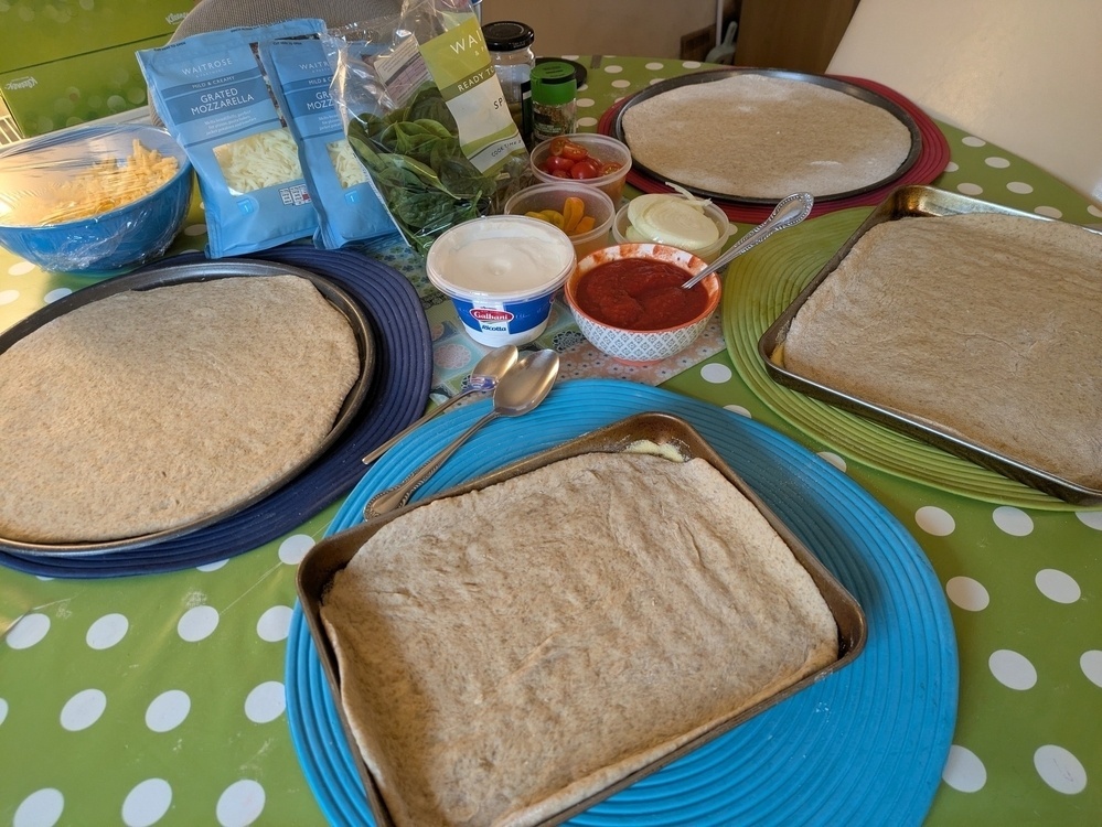 Pizza preparation setup with dough, cheese, sauces, and toppings on a polka dot tablecloth.