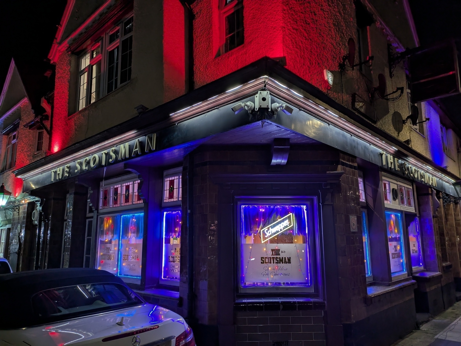 A corner building with bright neon lights and the name "The Scotsman" my local pub, photographed at night.