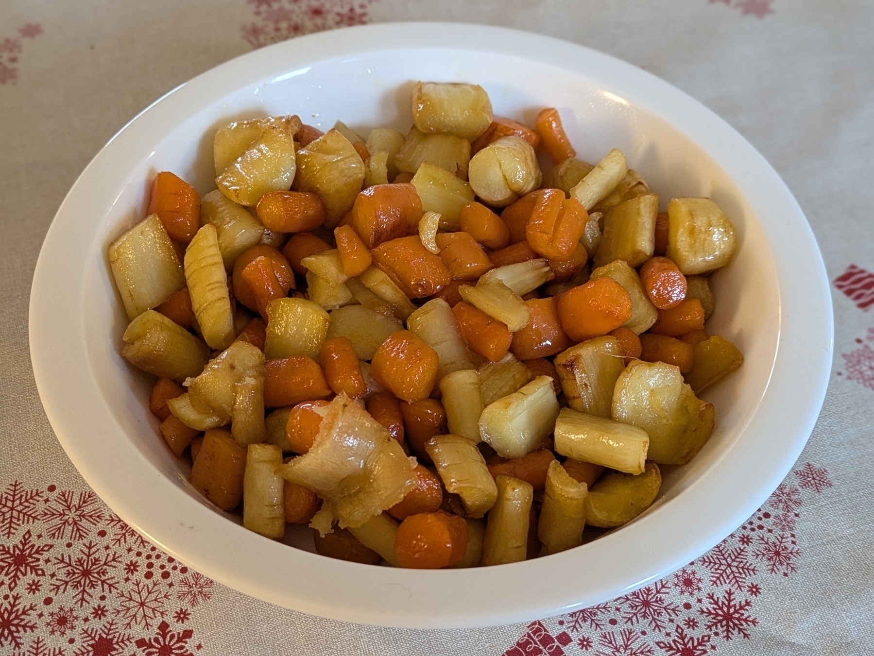 Auto-generated description: A bowl of honey-glazed carrots and parsnips sits on a patterned tablecloth.