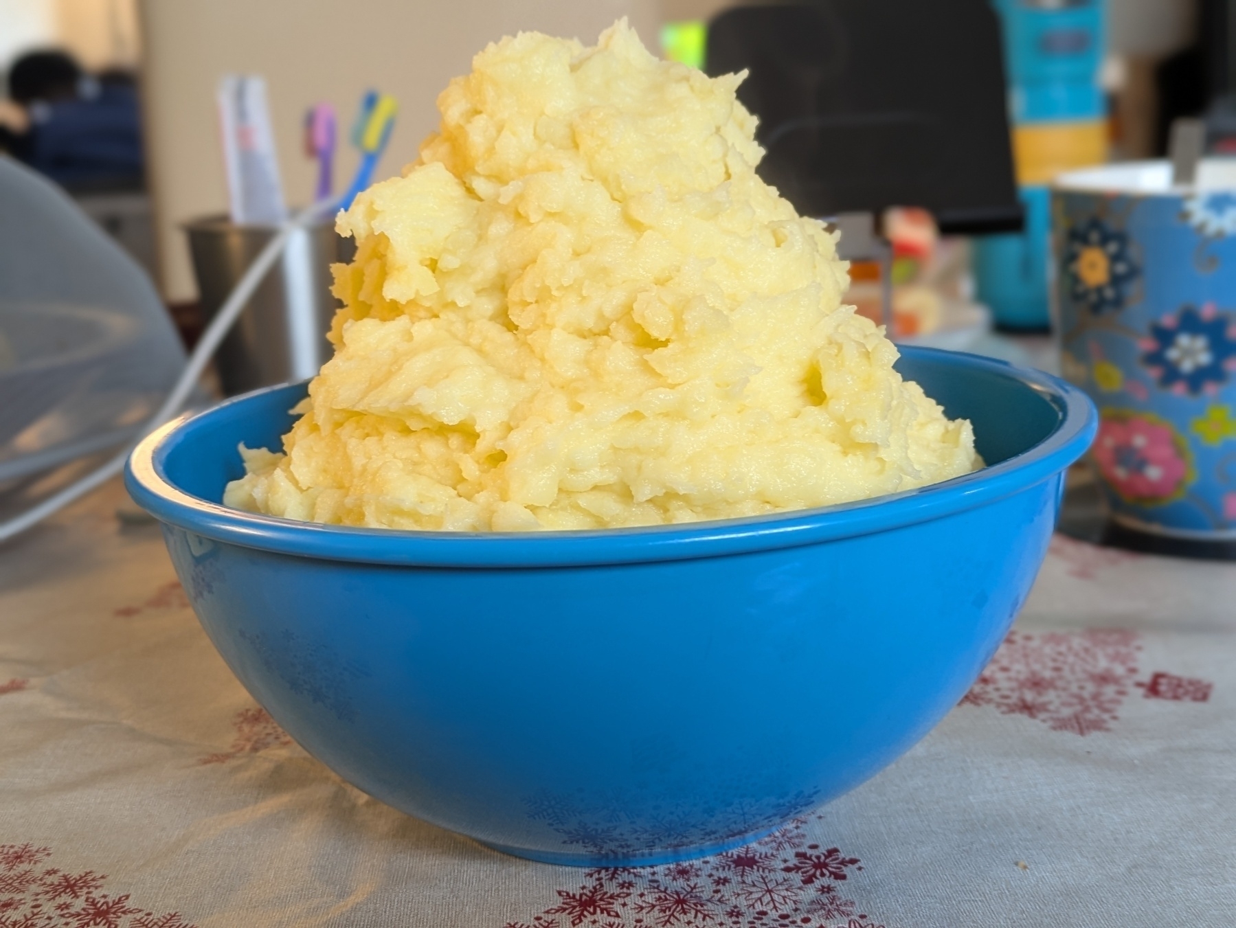 Auto-generated description: A large mound of mashed potatoes is heaped in a blue bowl on a table.