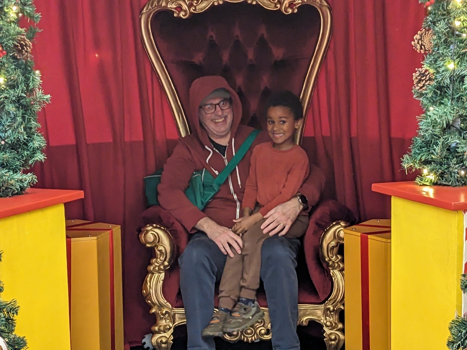 A person and a child are sitting together on an ornate chair surrounded by festive decorations.