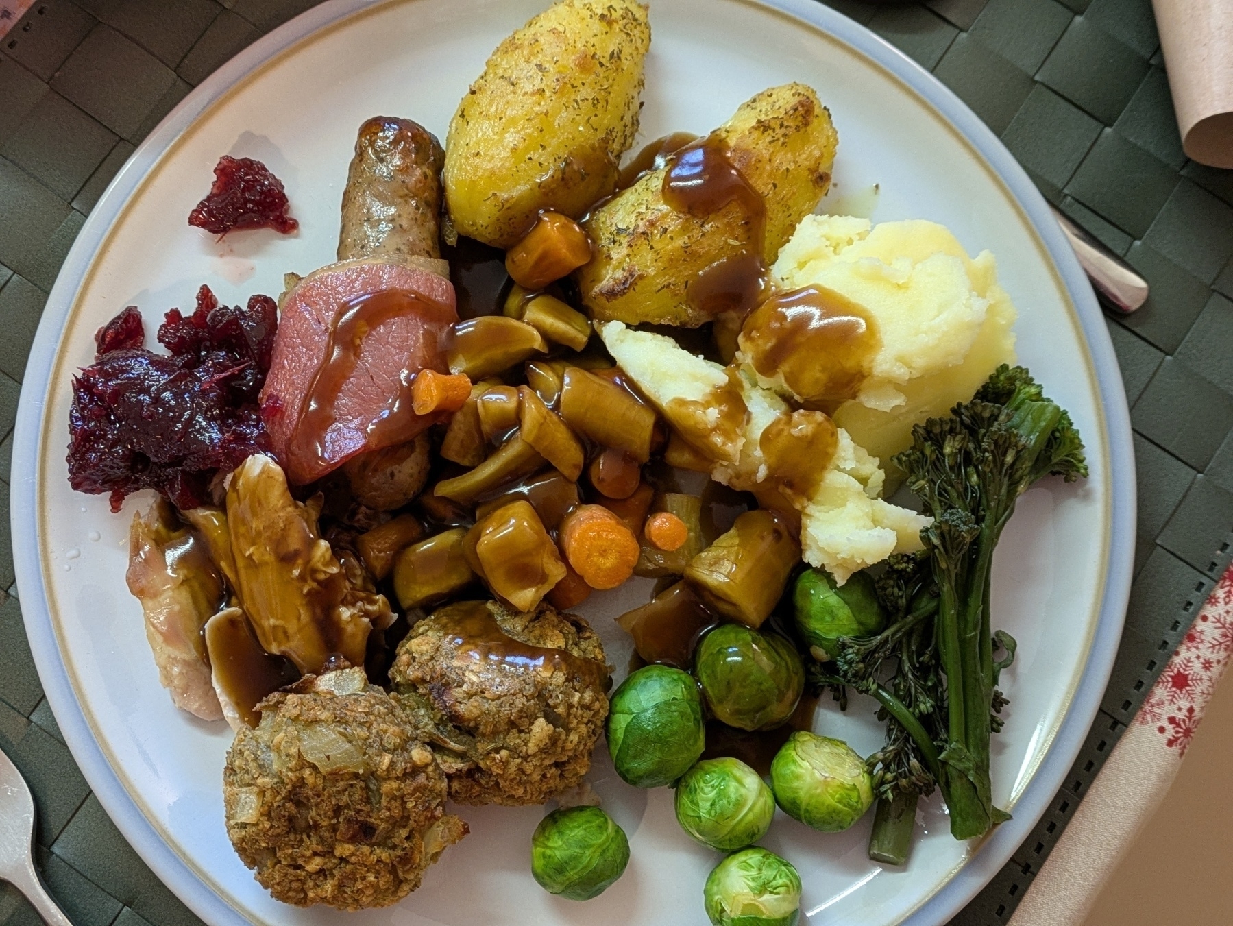 A plate is filled with a variety of foods including mashed potatoes, stuffing, brussels sprouts, broccoli, root vegetables, meat, and gravy.