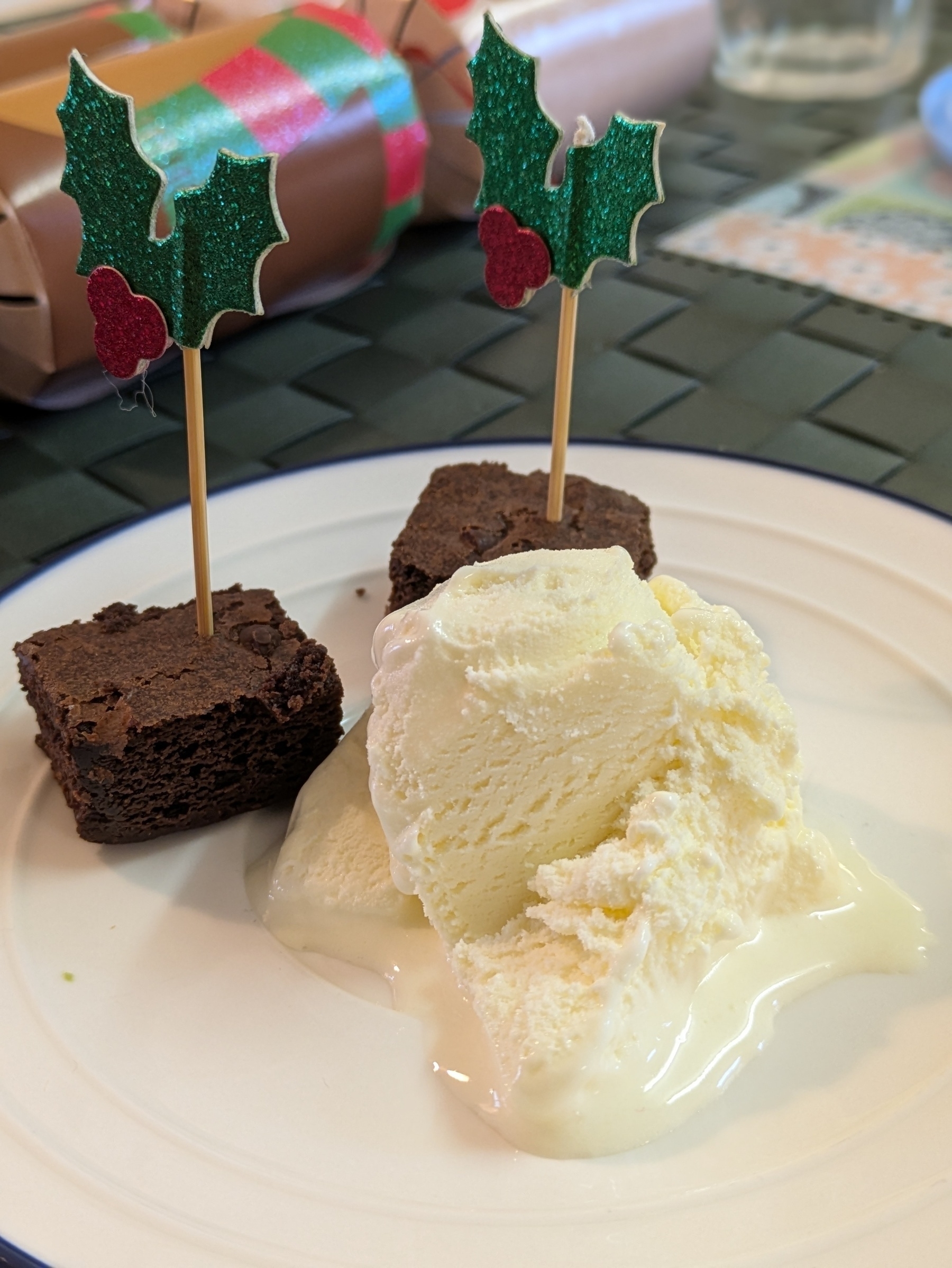 A plate features two pieces of chocolate brownie adorned with decorative holly picks and a serving of vanilla ice cream.