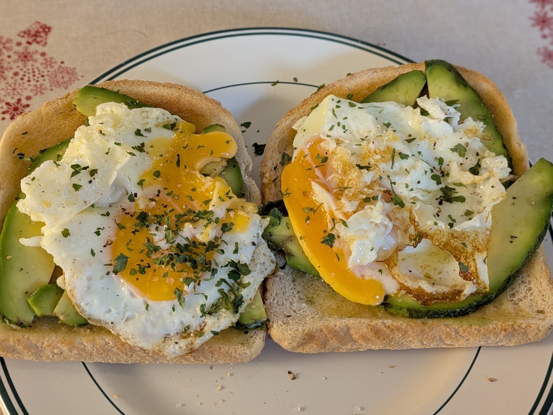 Two slices of bread topped with avocado, fried eggs, and herbs on a plate.