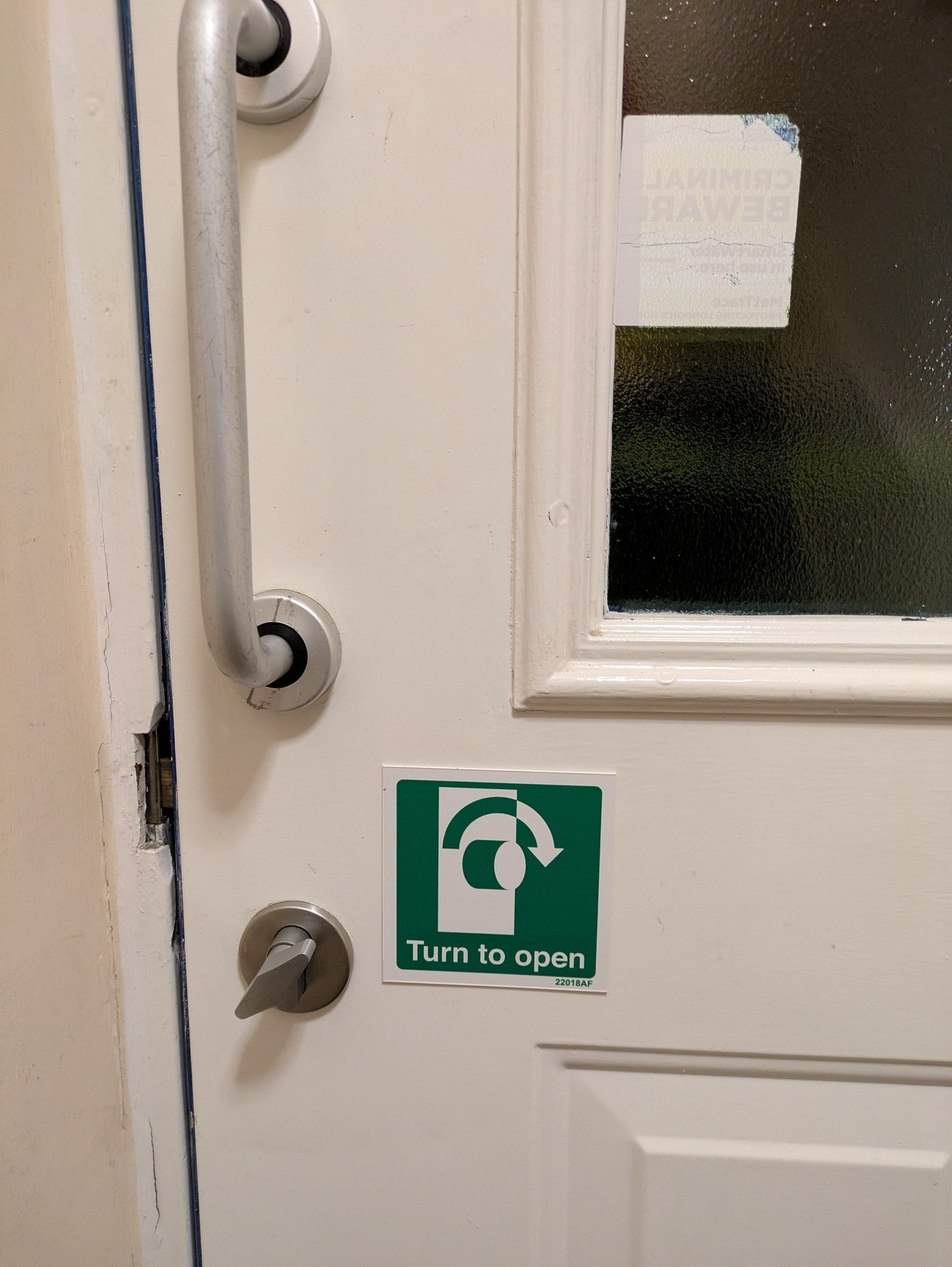 A door with a metal handle and lock features a green sign indicating "Turn to open."