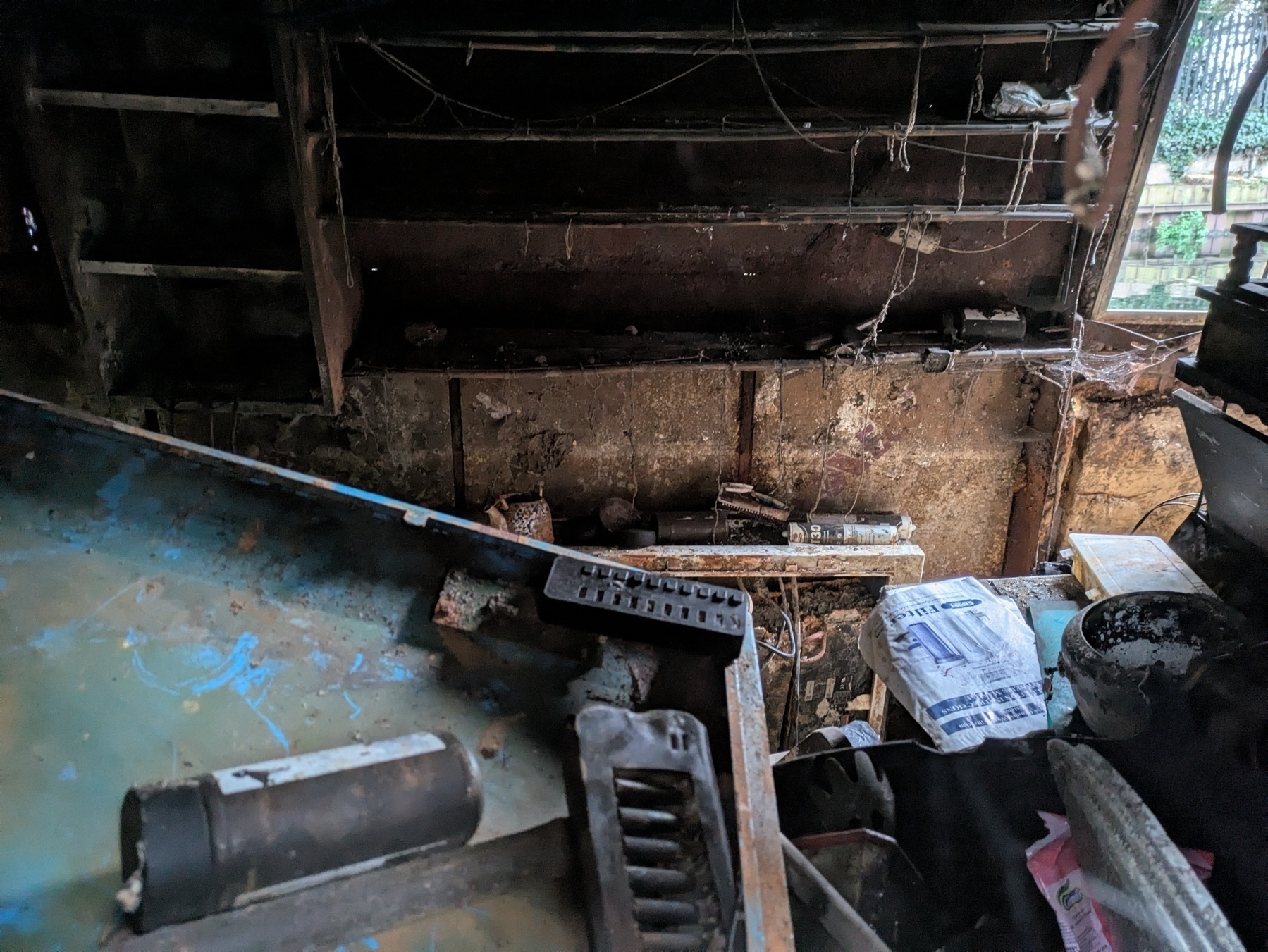 Auto-generated description: A cluttered, dimly lit room is filled with various discarded objects and debris, featuring peeling walls and exposed shelves, and a small noose.