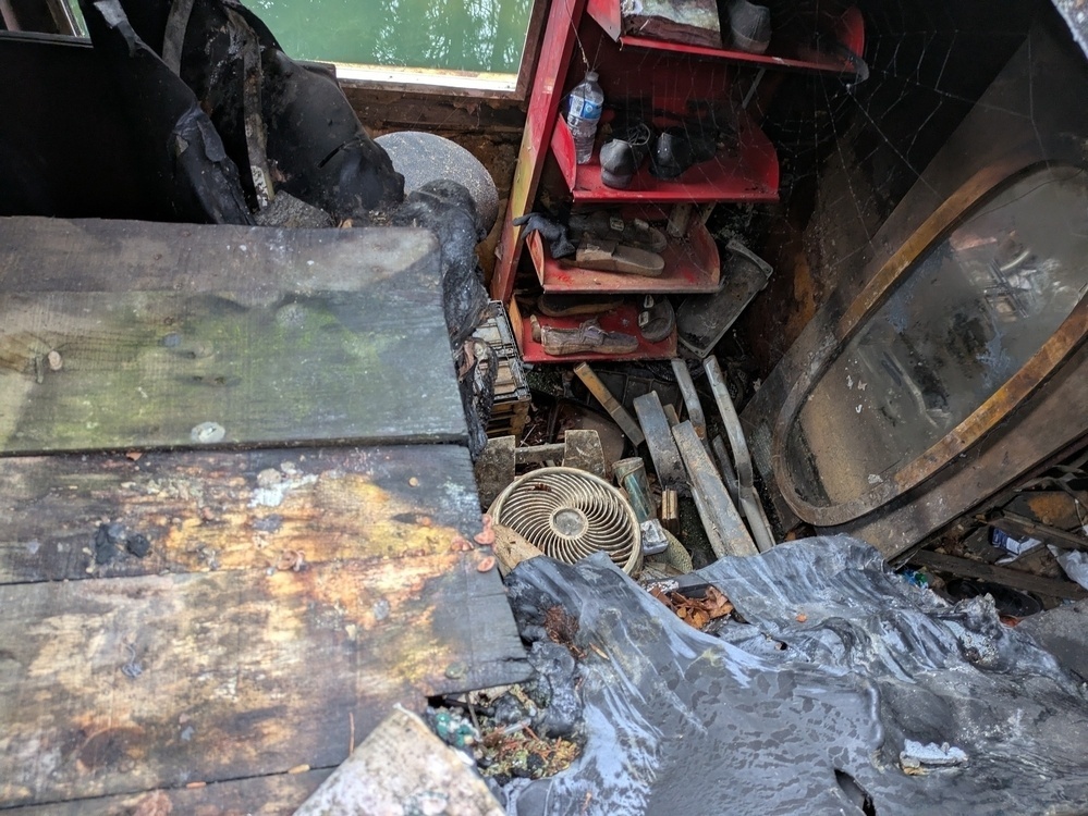 A cluttered space with charred debris, a damaged bathtub, and scattered household items is visible, indicating fire damage.