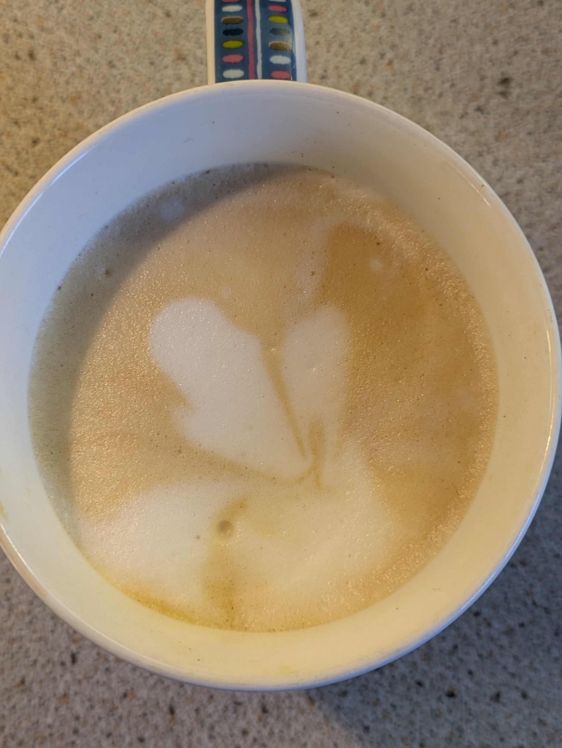 Auto-generated description: A cup of frothy coffee with an abstract latte art design on top sits on a textured surface.