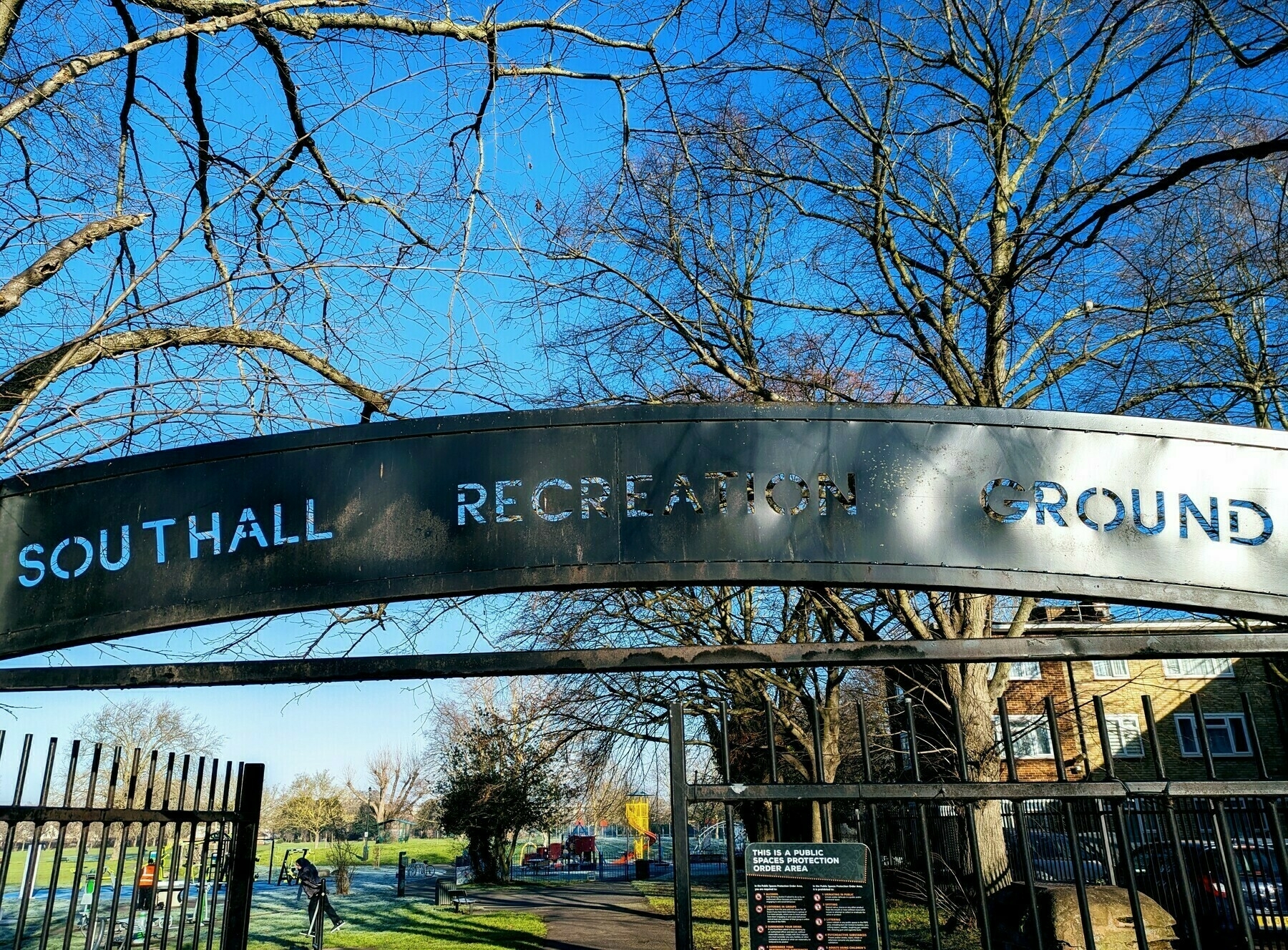 A metal archway sign reads Southall Recreation Ground situated above an entrance gate with trees and a path leading into the park area.