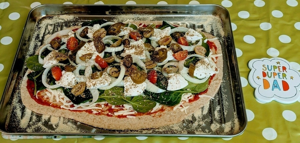 A homemade pizza topped with vegetables and cheese is placed on a baking tray with a Super Duper Dad card beside it.