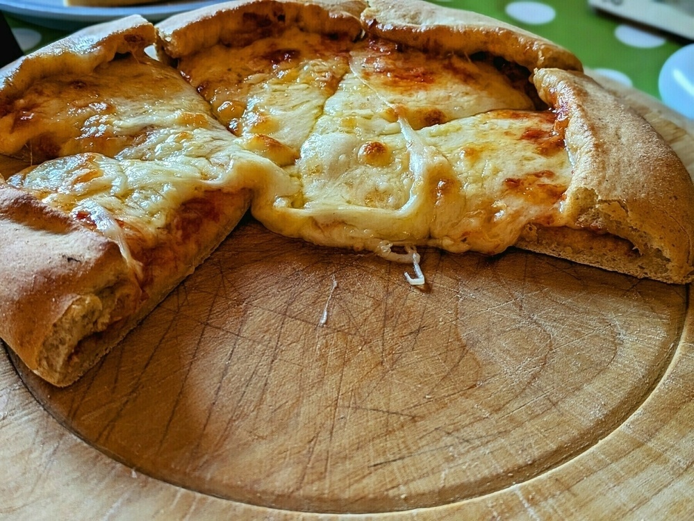 A cheesy pizza with melted cheese is partially sliced on a wooden board.