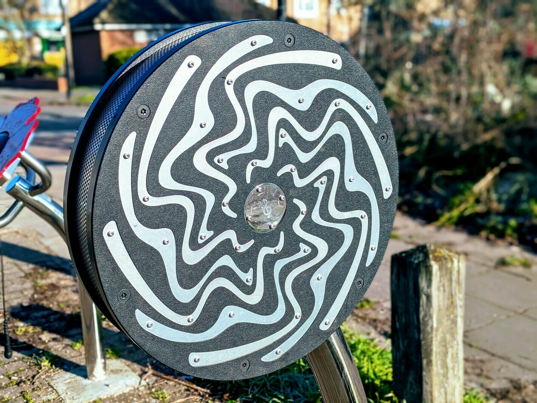 A circular object with wavy white lines on a textured black background is mounted on a metal stand in an outdoor setting.