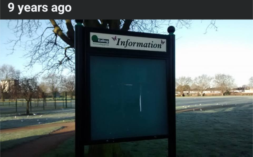 Auto-generated description: A frosty park landscape features an empty information board with trees and a path in the background.