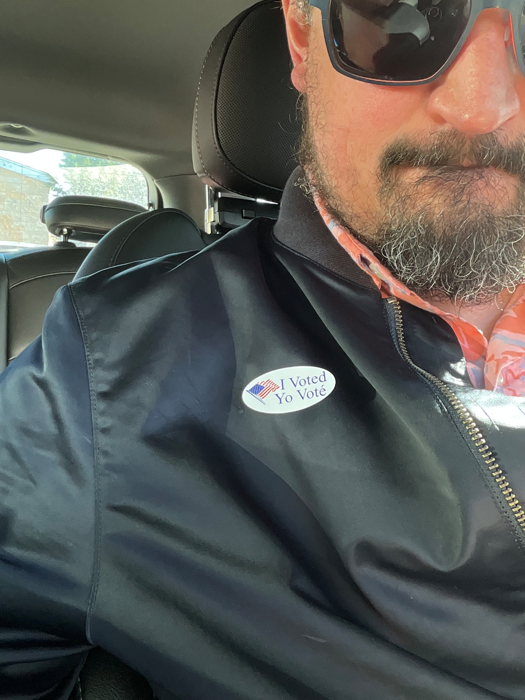I am sitting on my car wearing a sticker that says “I voted / Yo voté”
