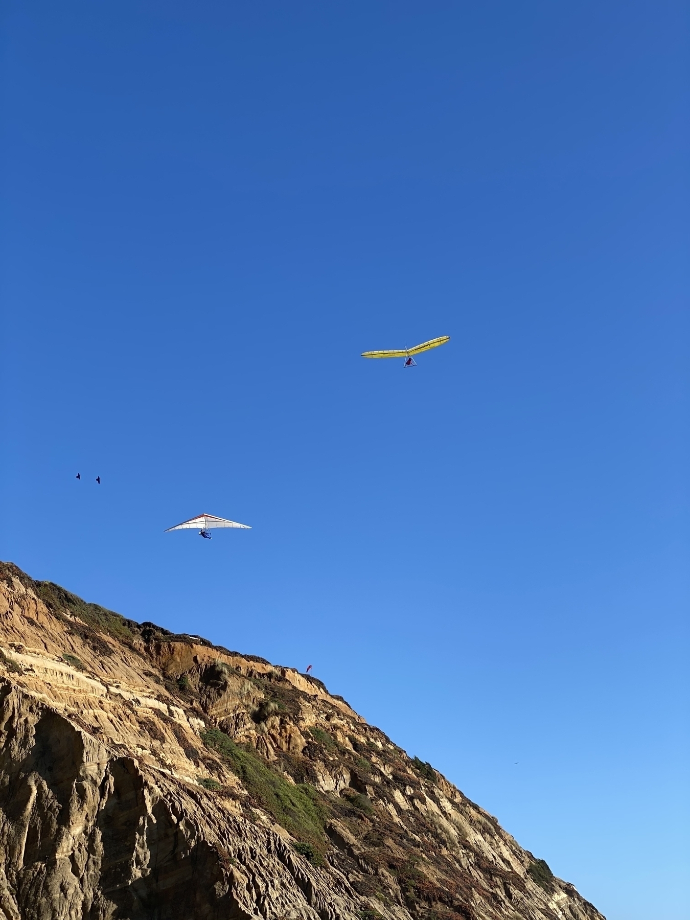 Two hang gliders near a hill flying on a blue sky 