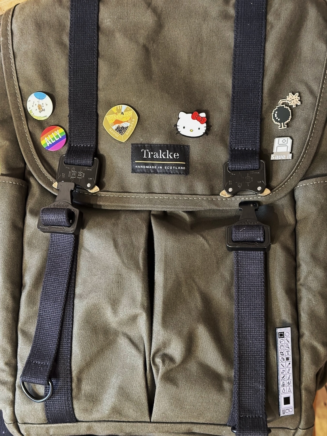 A backpack with several pins and badges attached to its outer flap, including a Hello Kitty"