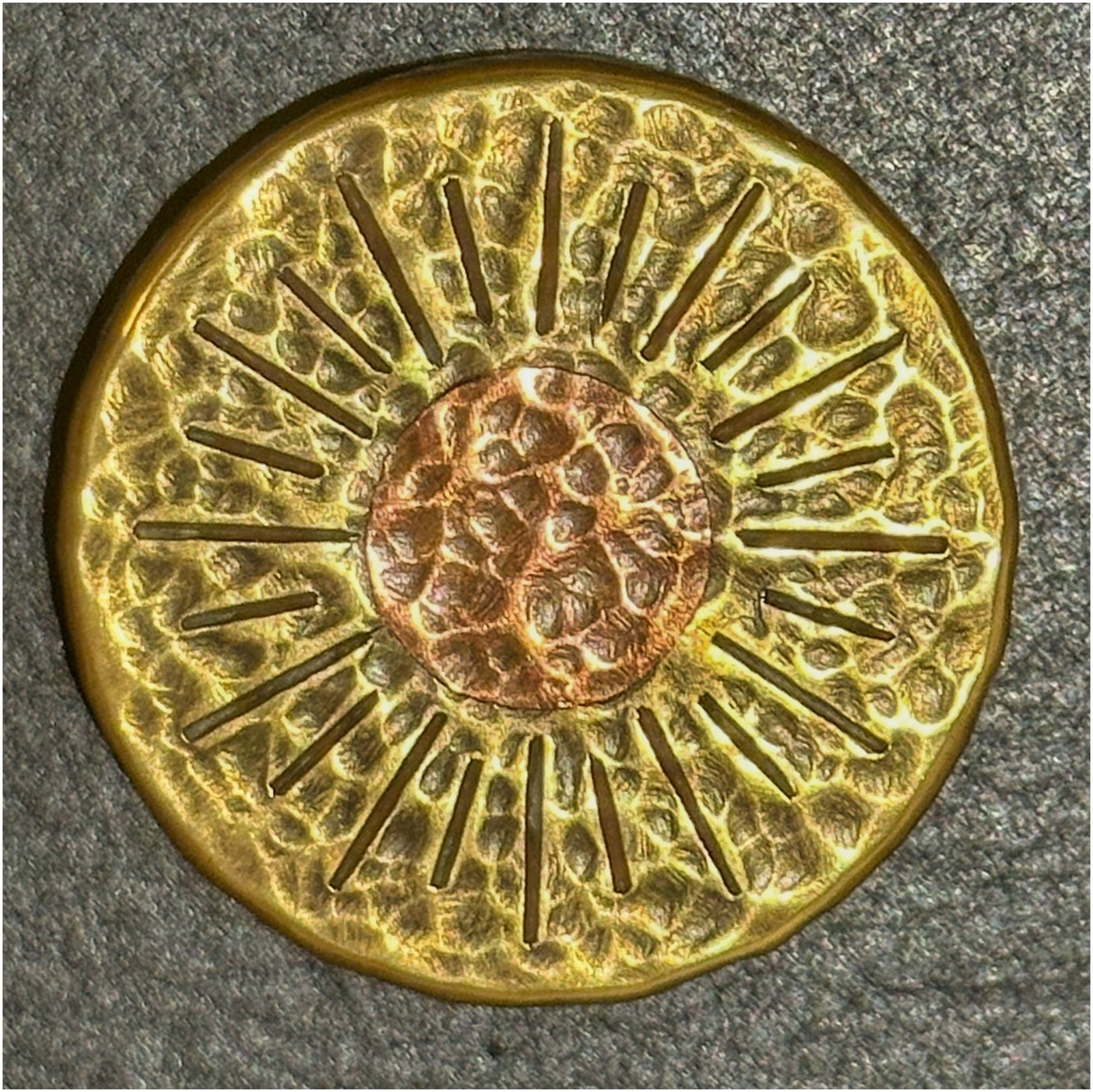 A close-up of a decorative, gold-colored round object with embossed radial patterns centered around a circular motif.
